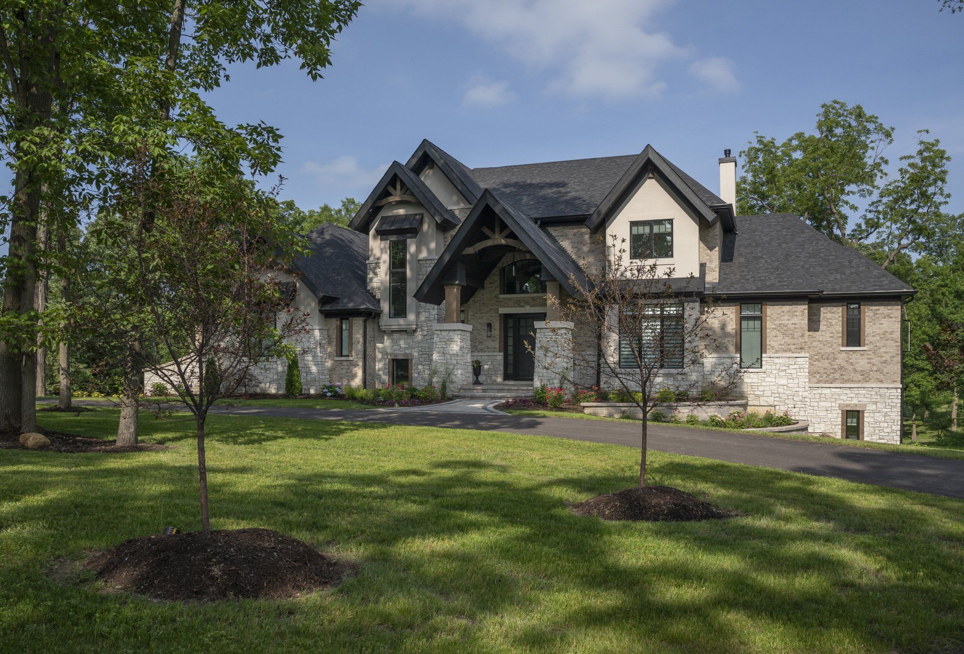 A large house is sitting on top of a lush green lawn surrounded by trees.