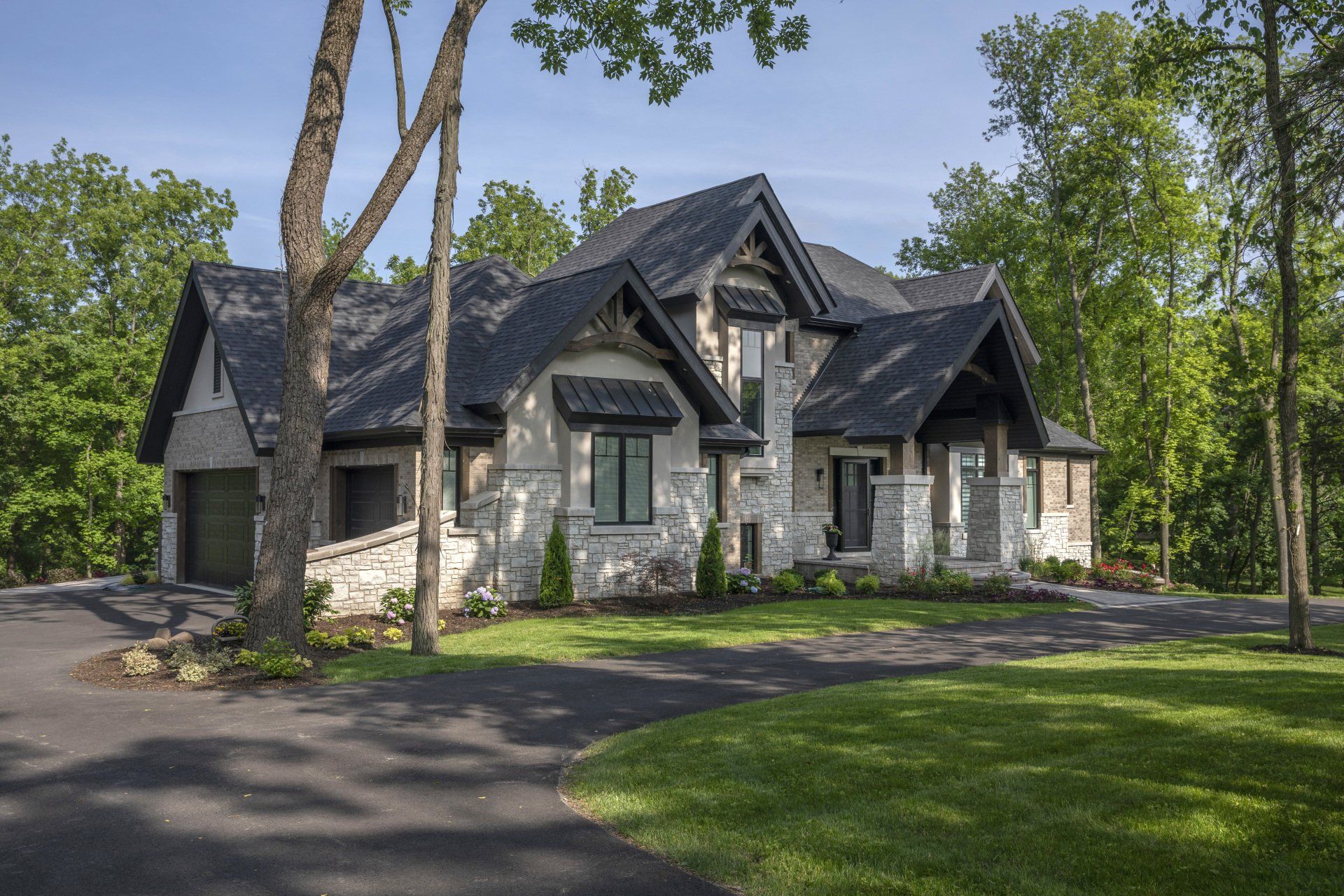 A large house with a black roof is surrounded by trees and grass.