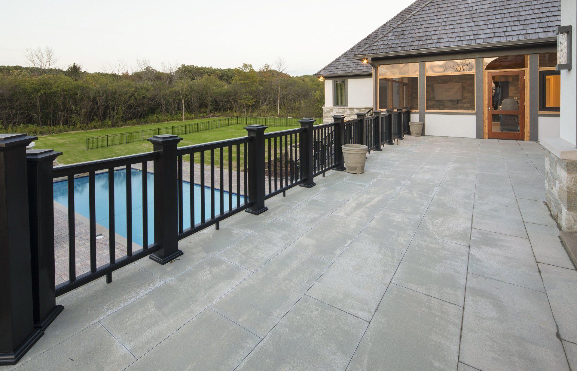 A patio with a black railing and a pool in the background