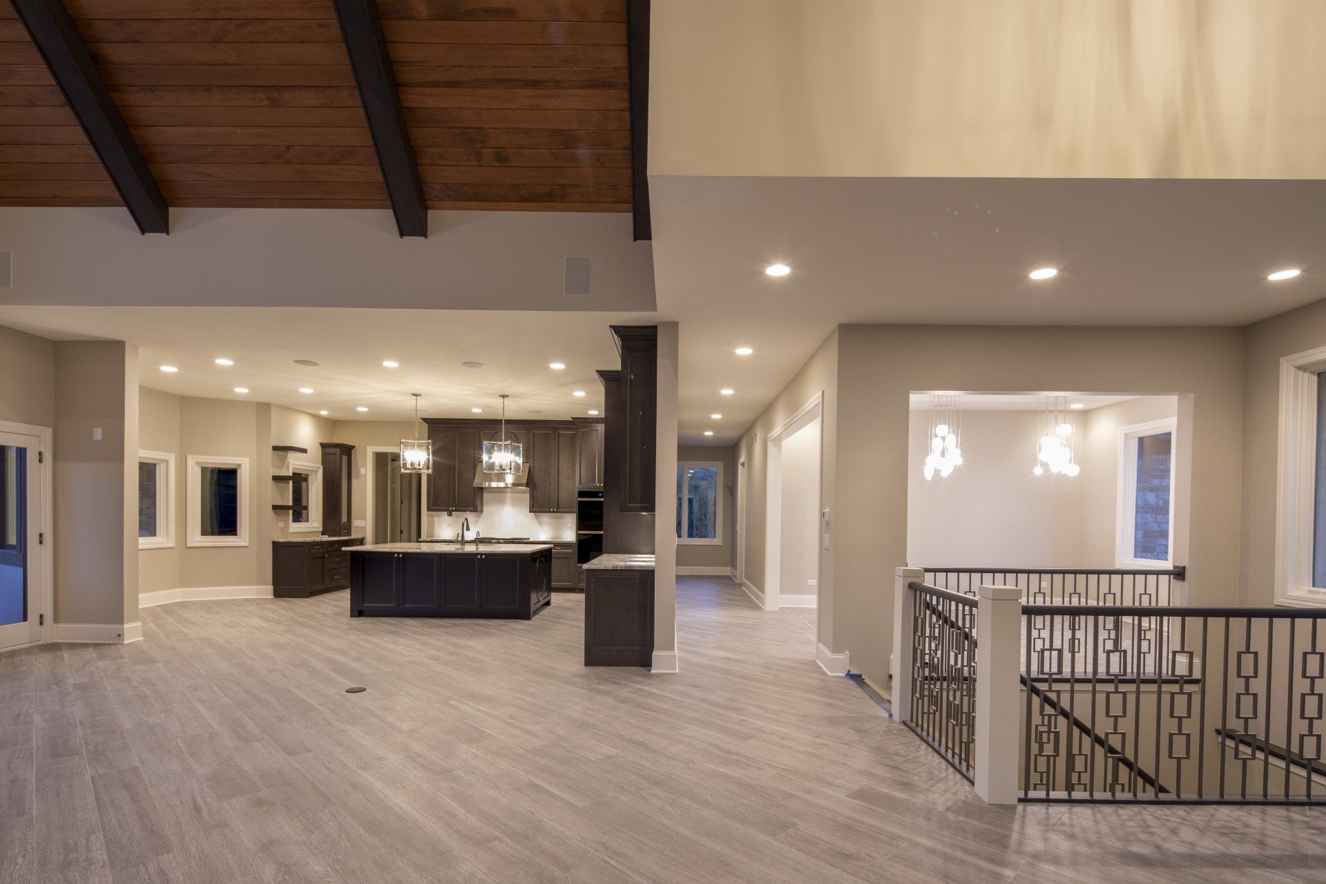 A large empty room with a wooden ceiling and a staircase leading to a kitchen.