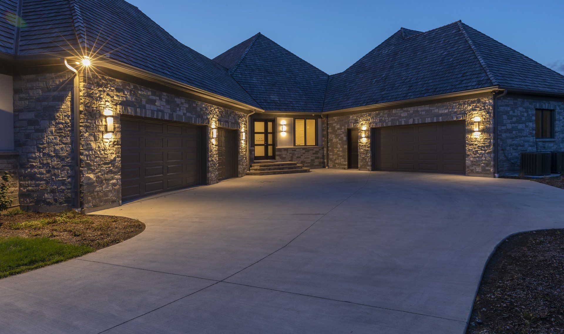 A large house with two garages and a driveway is lit up at night.