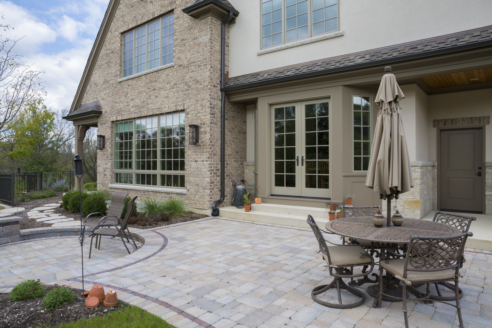 A patio with a table and chairs and an umbrella in front of a large house.