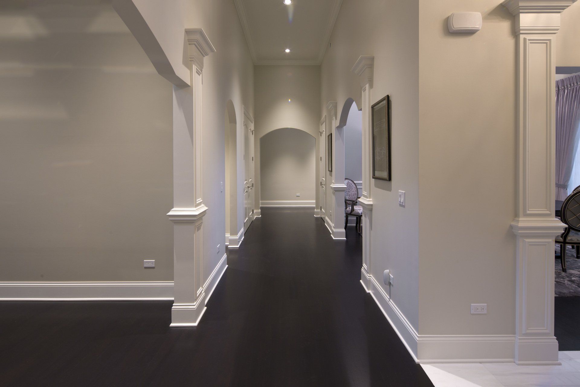A long hallway in a house with white walls and black floors.