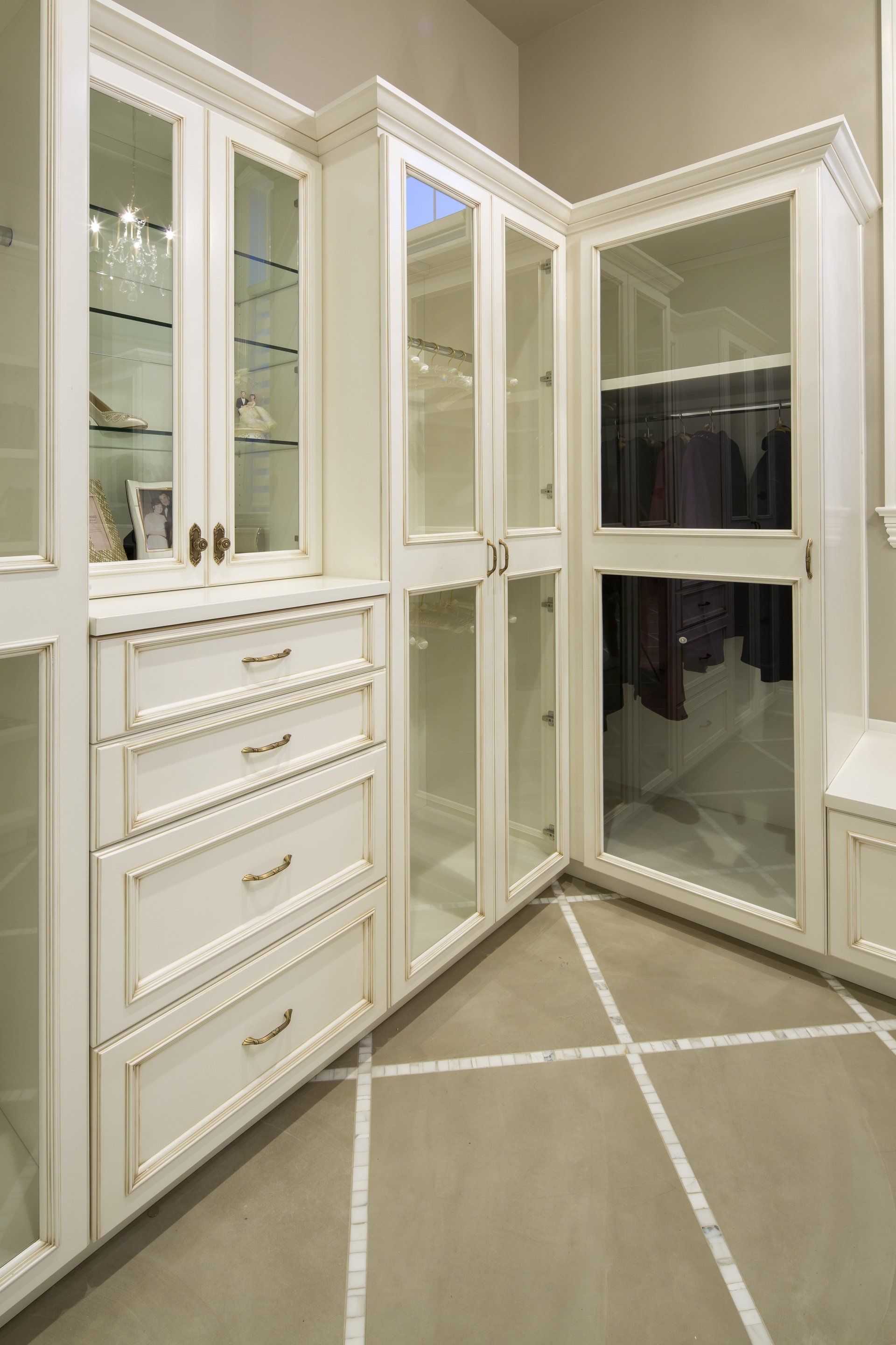 A walk in closet with white cabinets and glass doors.