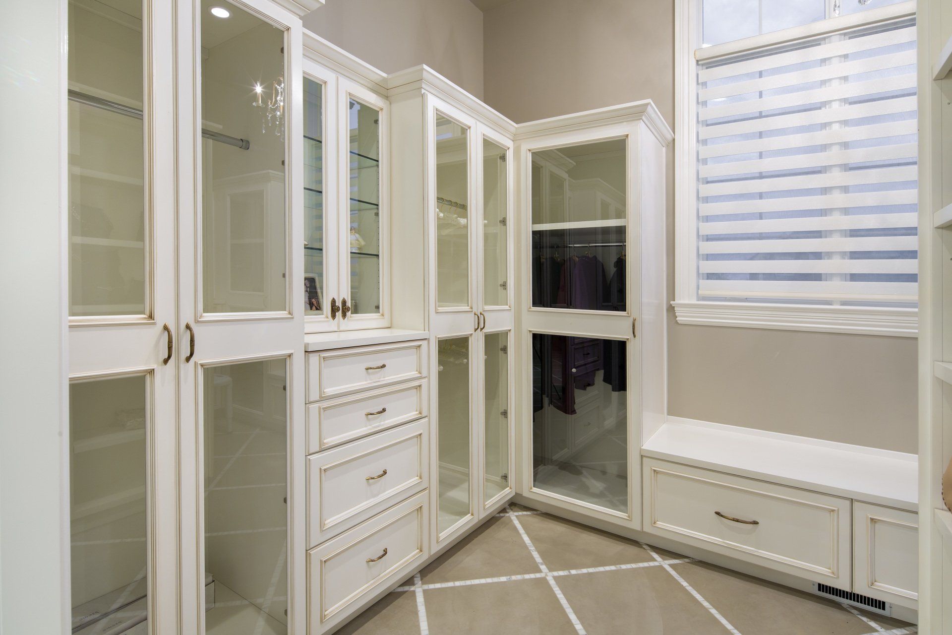 A walk in closet with white cabinets and glass doors.
