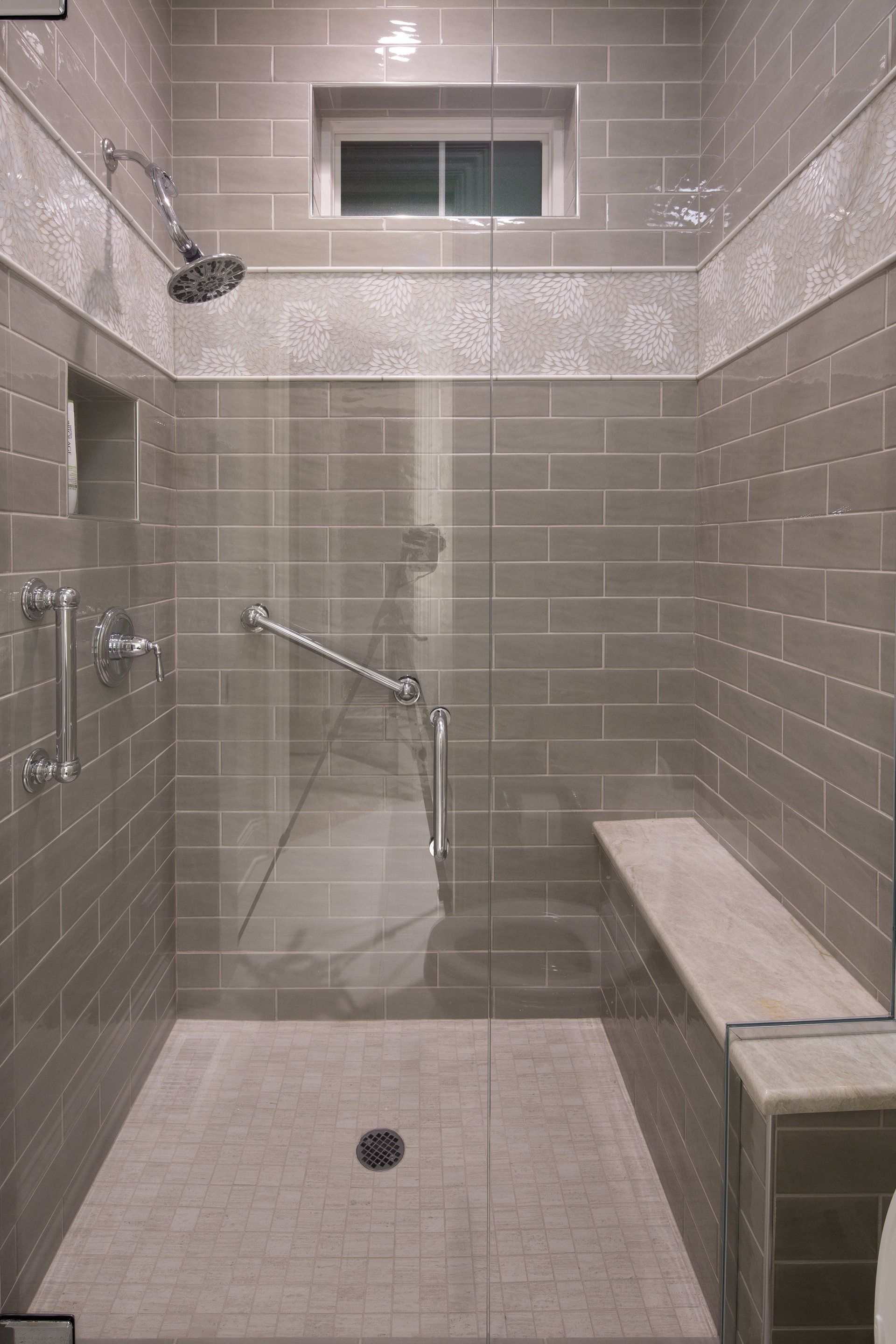 A bathroom with a walk in shower with a glass door and a bench.