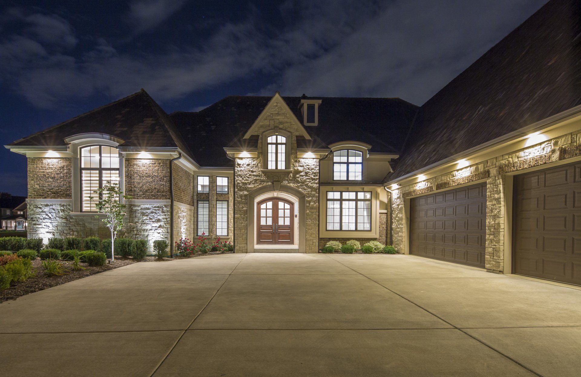 A large brick house with a large driveway is lit up at night.