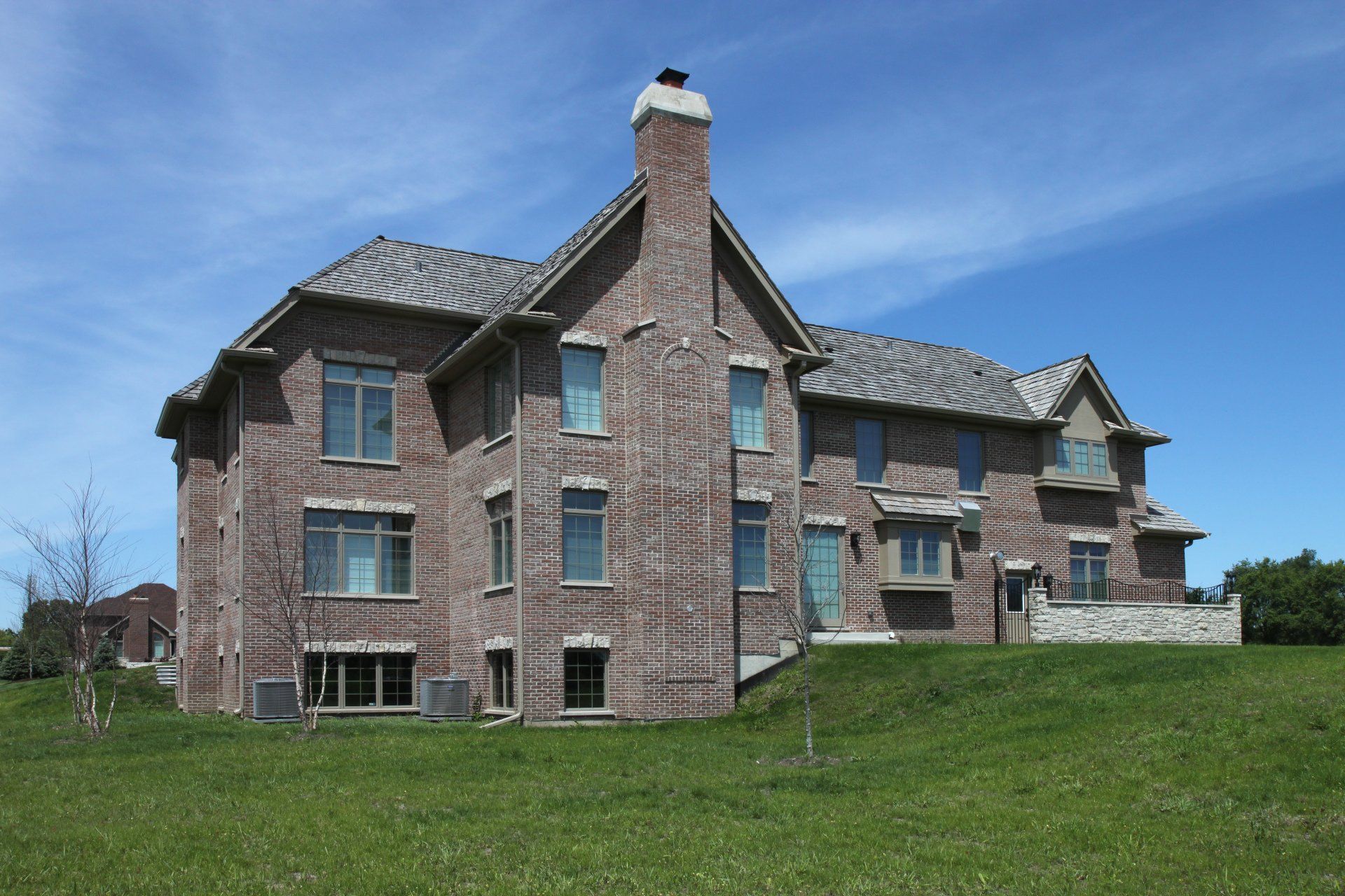 A large brick house sits on top of a grassy hill