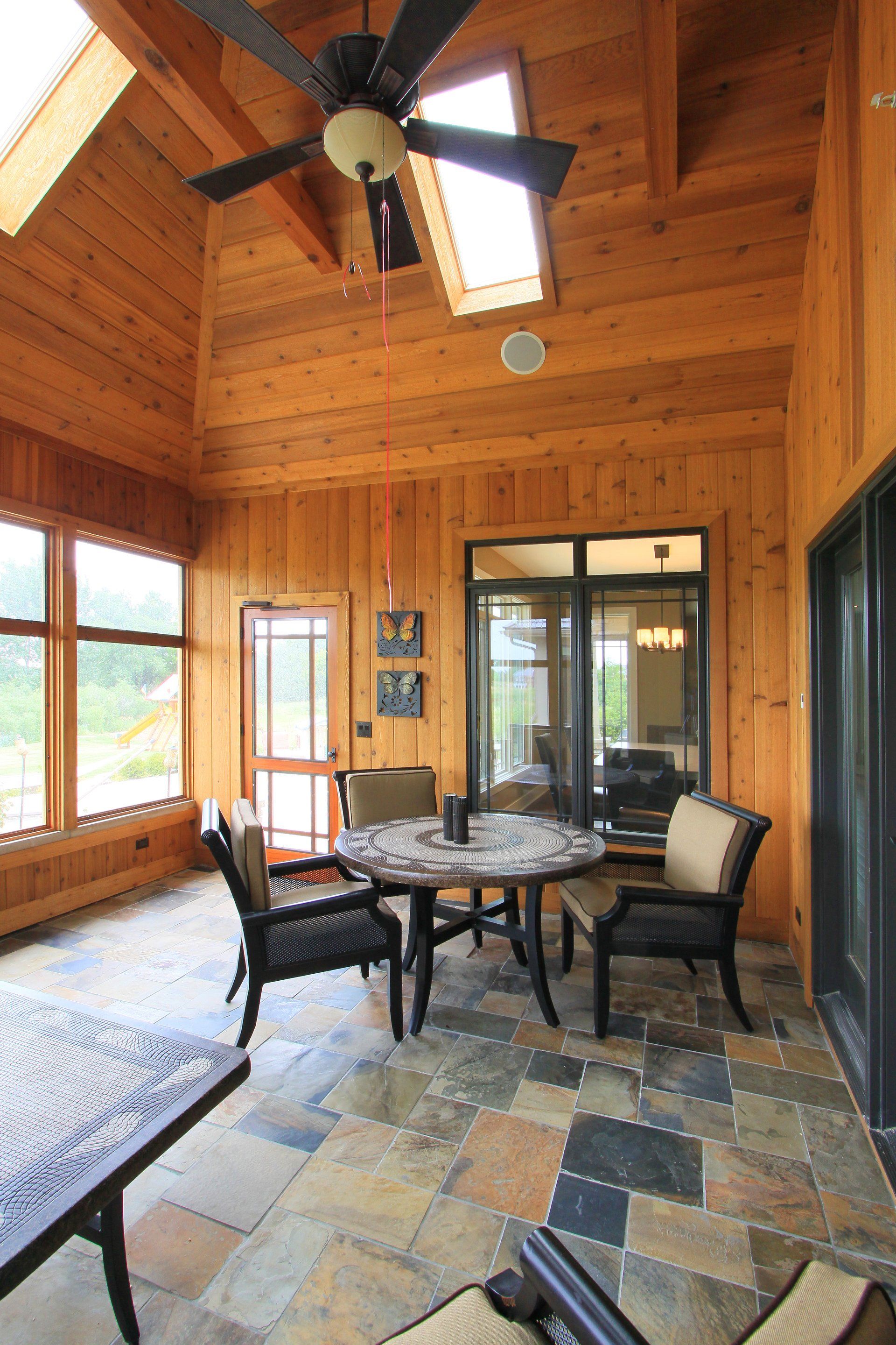 A screened in porch with a table and chairs and a ceiling fan