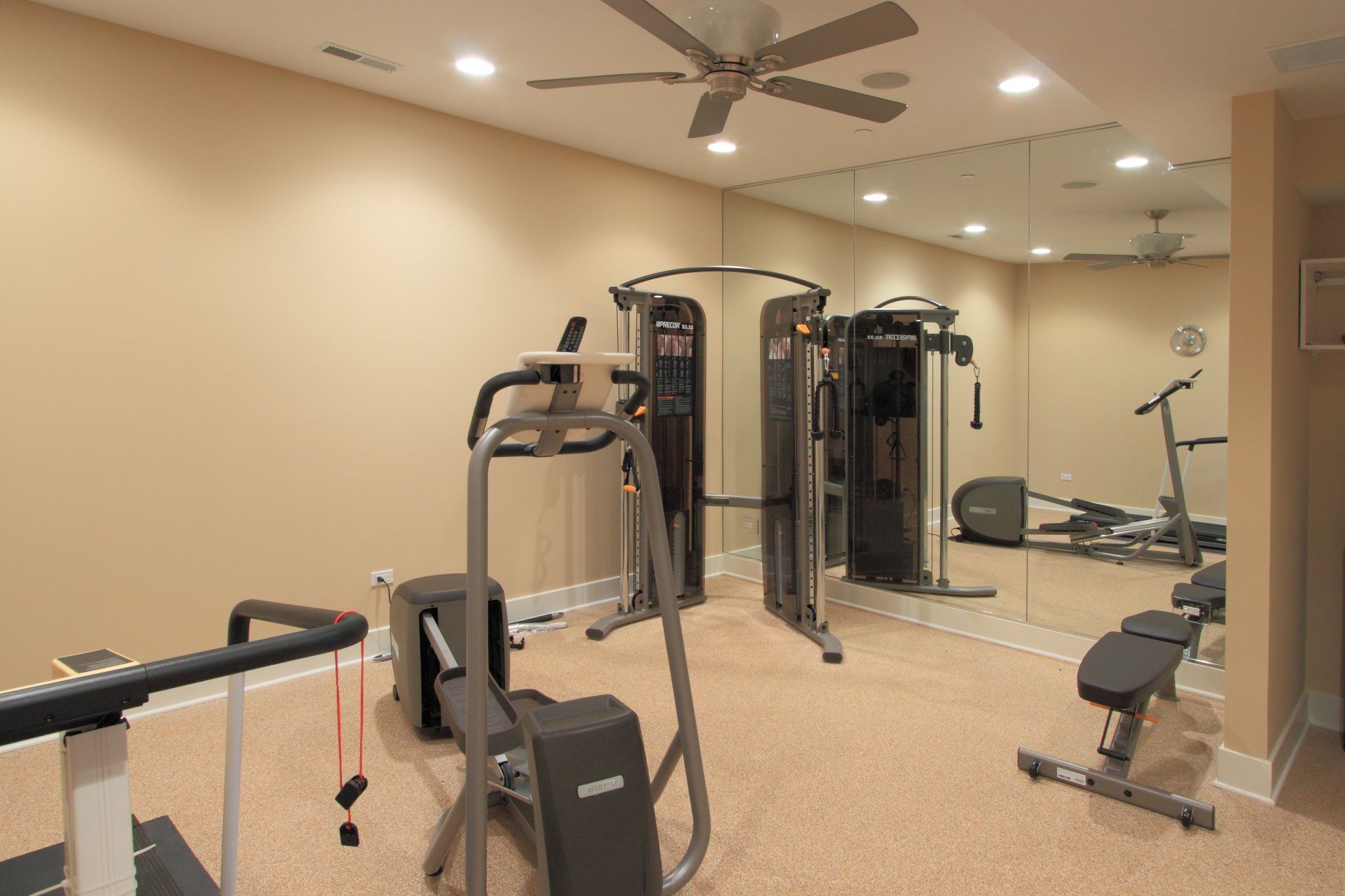 A gym with a lot of equipment and a ceiling fan