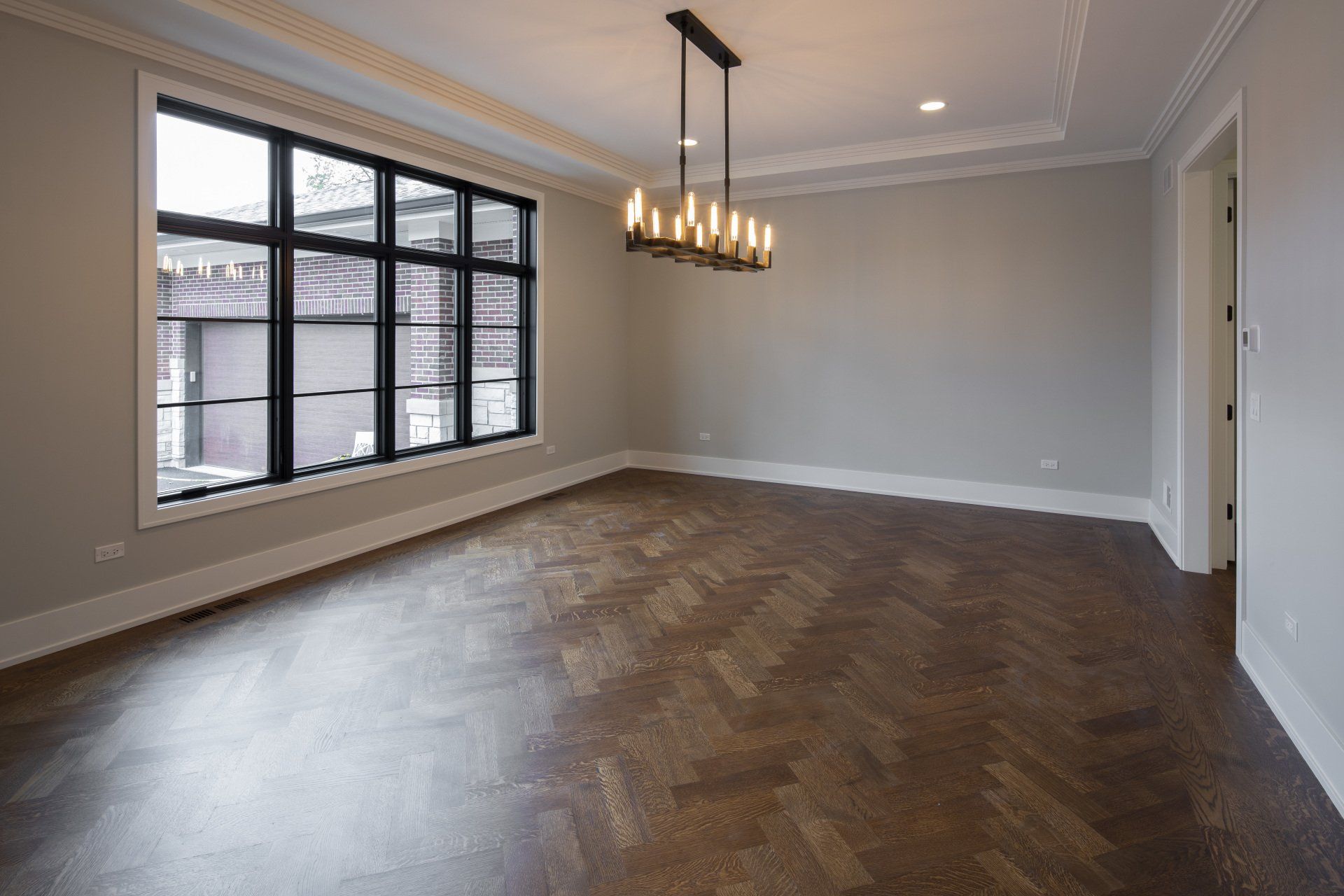 An empty living room with hardwood floors and a chandelier hanging from the ceiling.