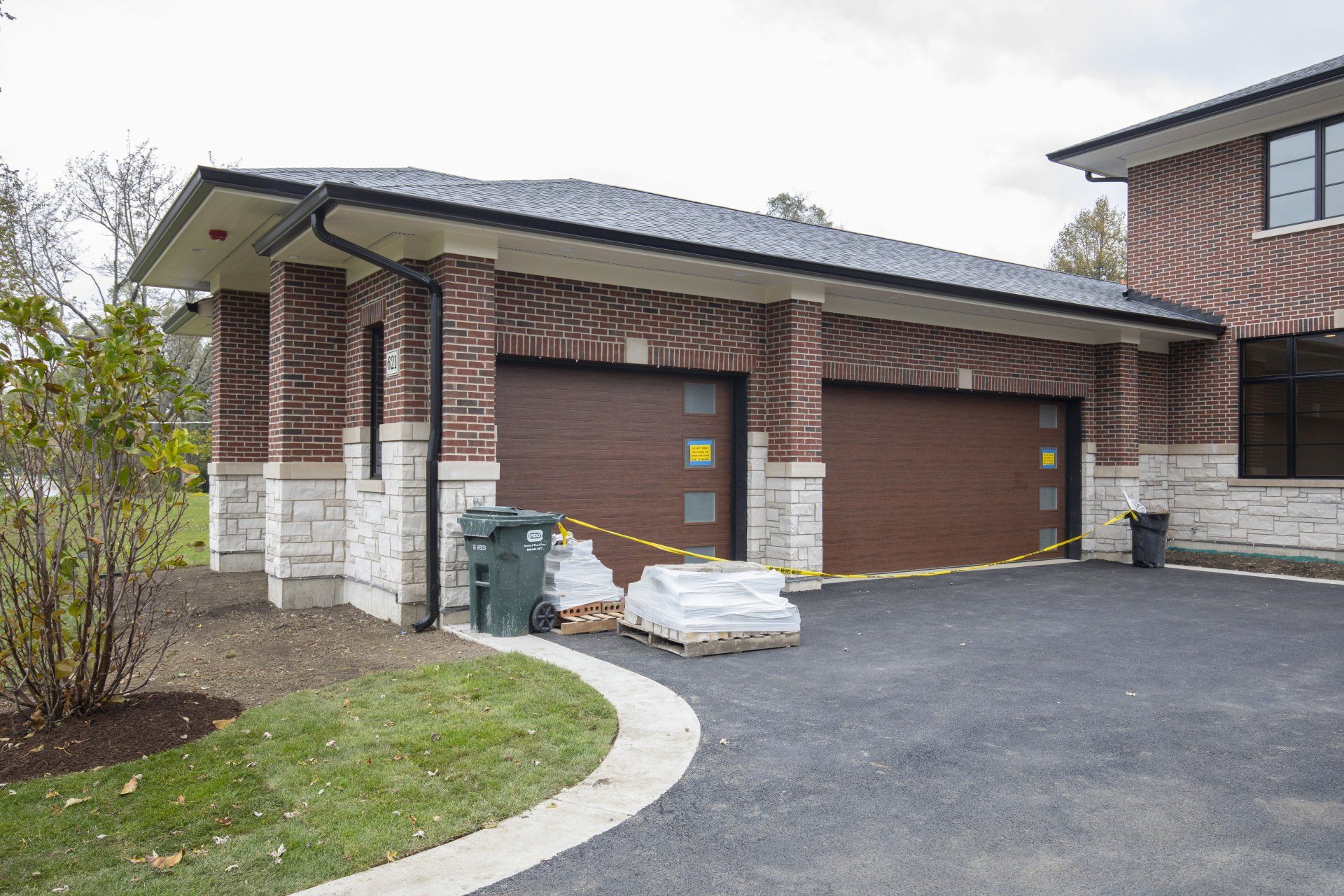 A brick house with two garage doors and a trash can in front of it.