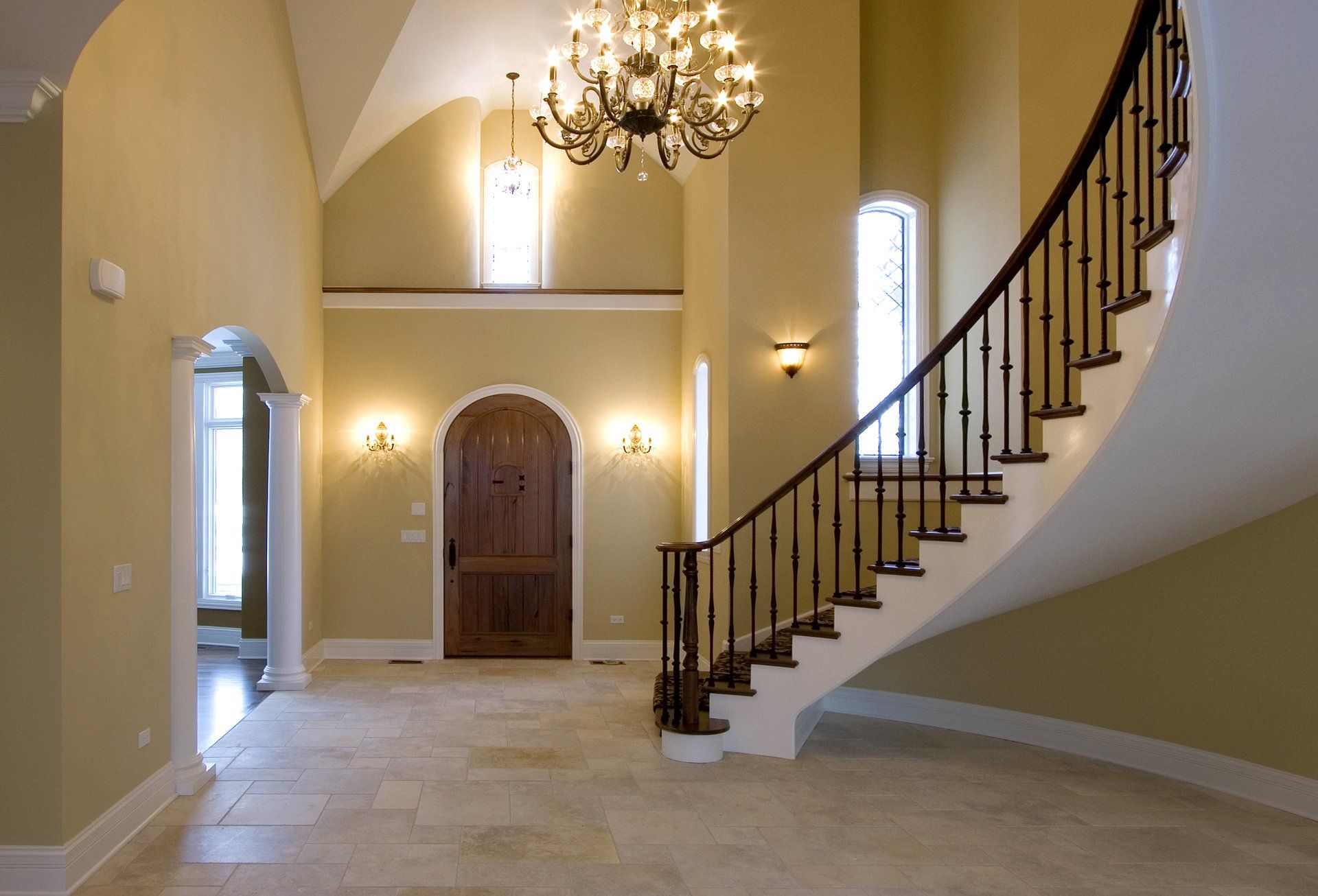 An empty hallway with a curved staircase and a chandelier