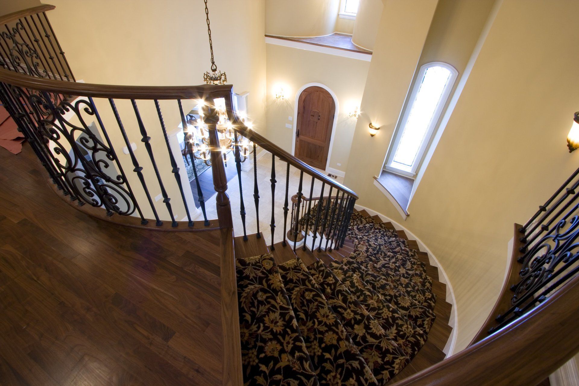 A spiral staircase with a wrought iron railing and a chandelier hanging from the ceiling.