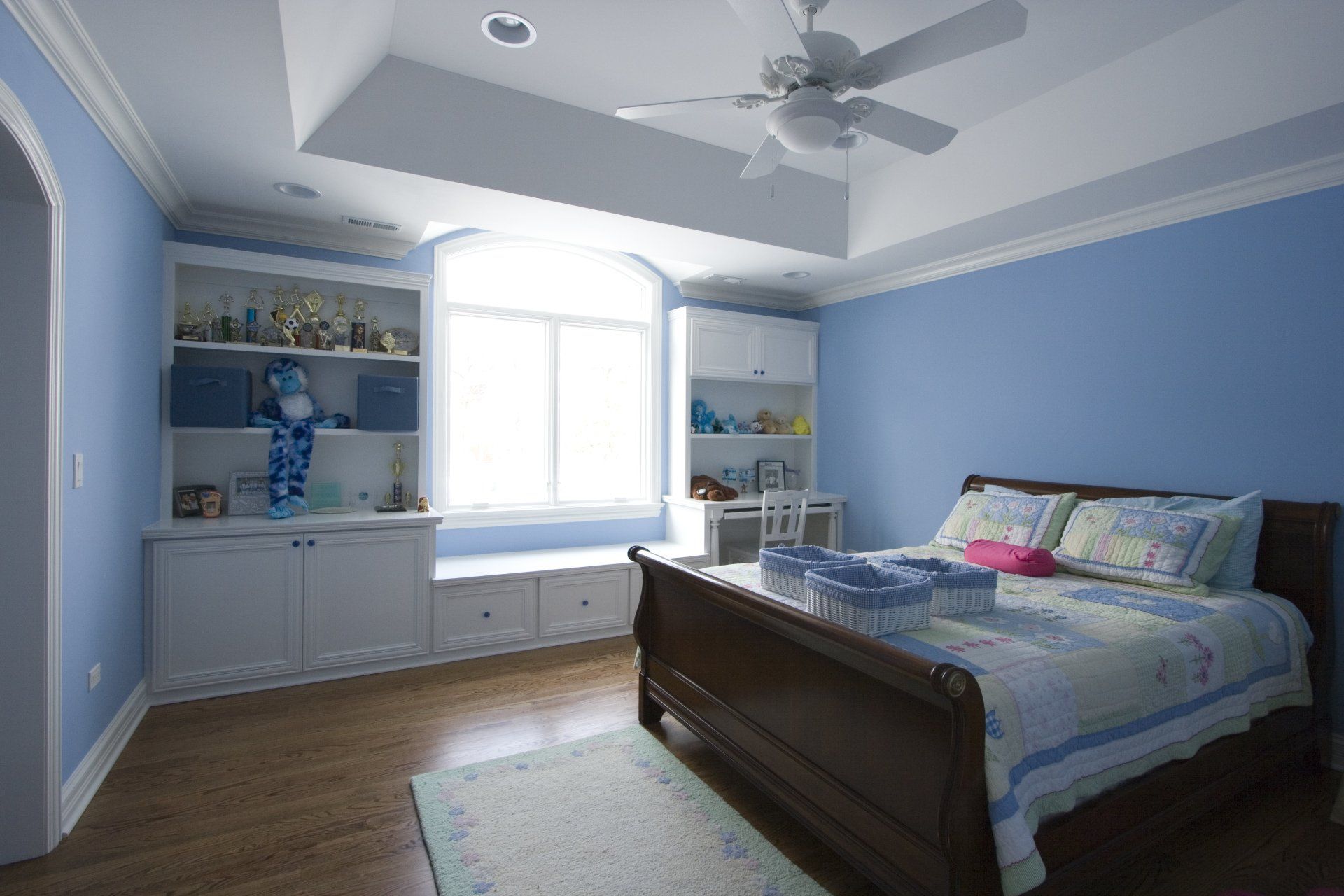 A bedroom with blue walls , a bed , a ceiling fan and a window.