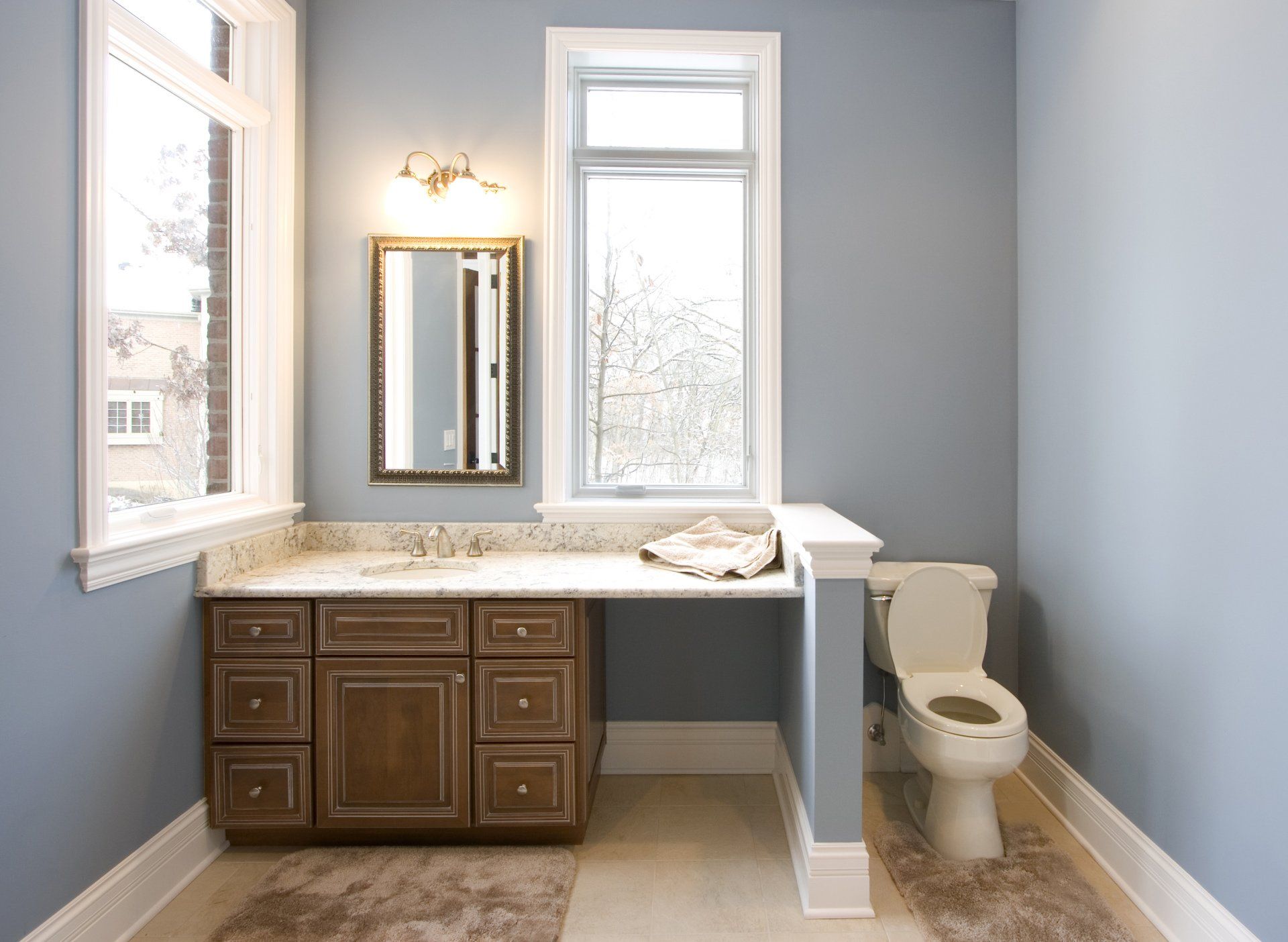 A bathroom with a toilet , sink , mirror and window.