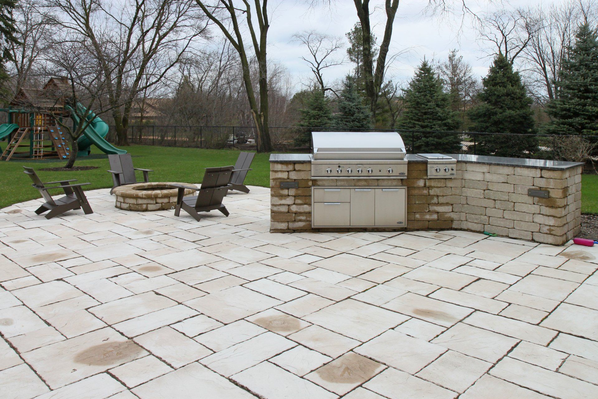A patio with a grill and chairs and a playground in the background