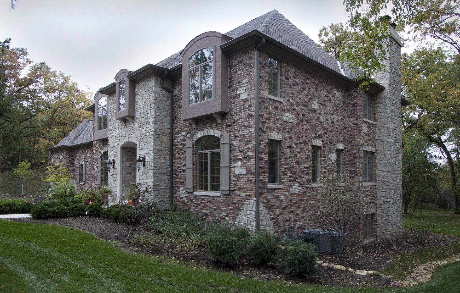 A large brick house with a lot of windows is surrounded by trees.