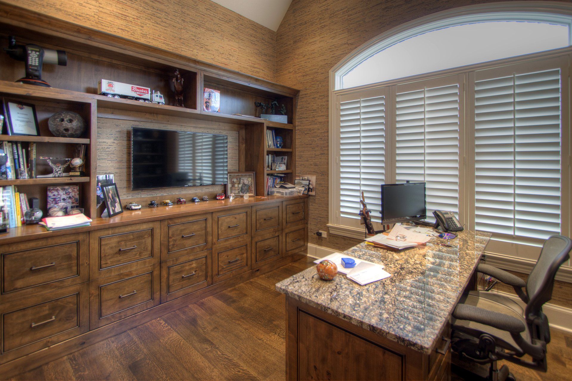 A home office with a desk , chairs , shelves and a television.
