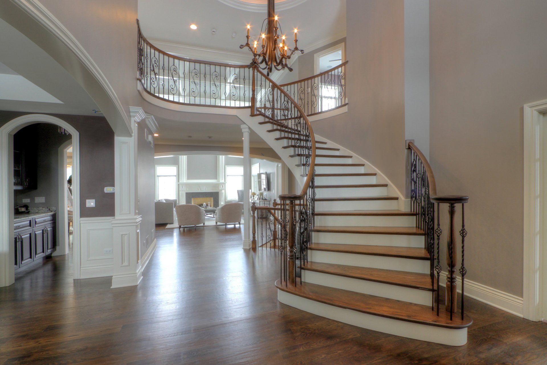 A curved staircase in a large house with a chandelier hanging from the ceiling.