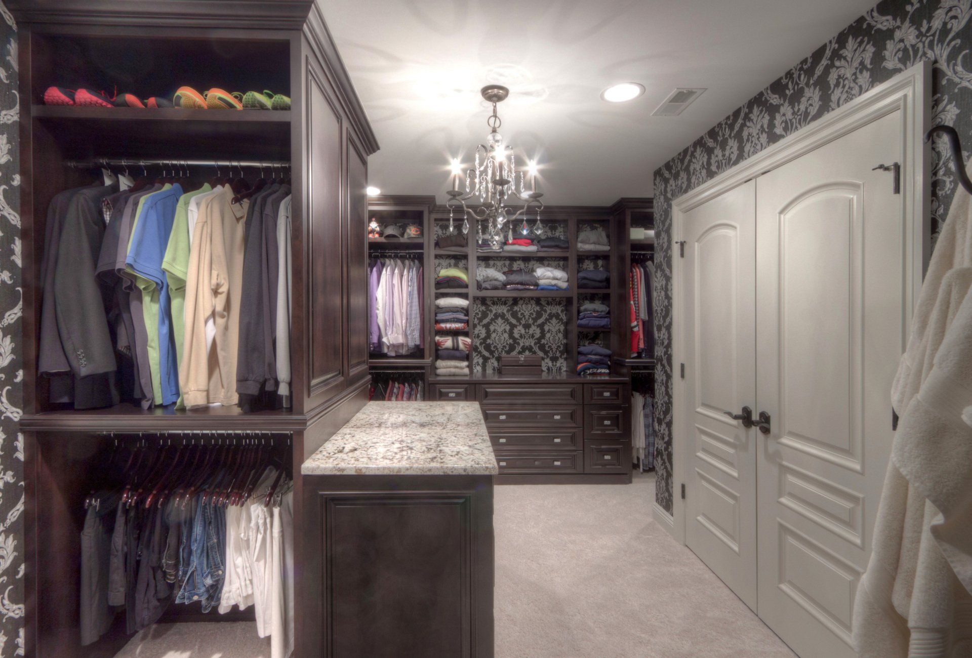 A large walk in closet with lots of clothes and a chandelier.