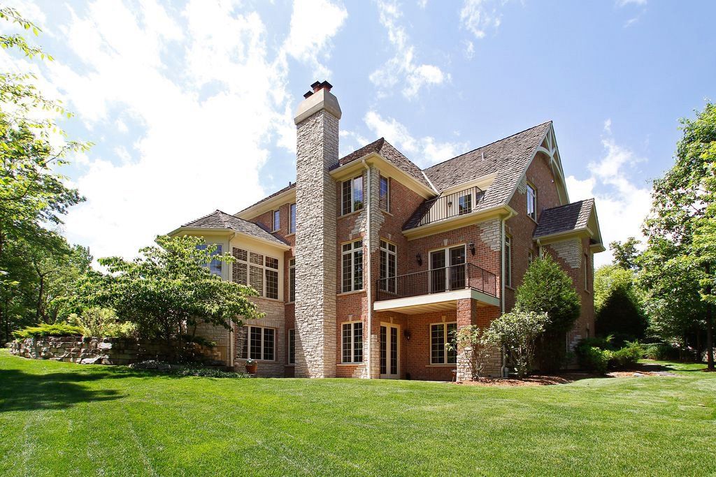 A large brick house with a stone chimney is sitting on top of a lush green lawn.