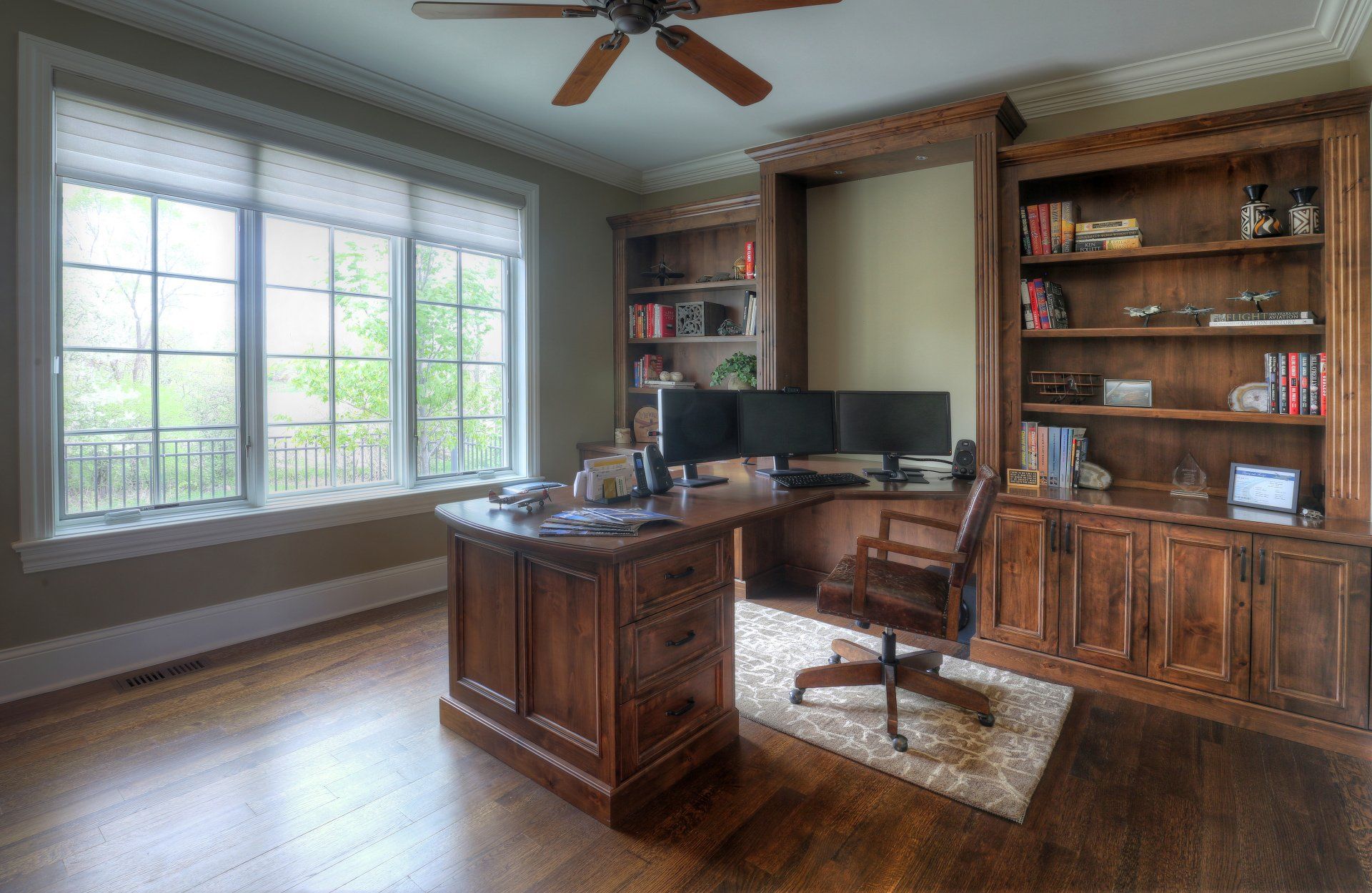A home office with a desk , chair , shelves and a ceiling fan.