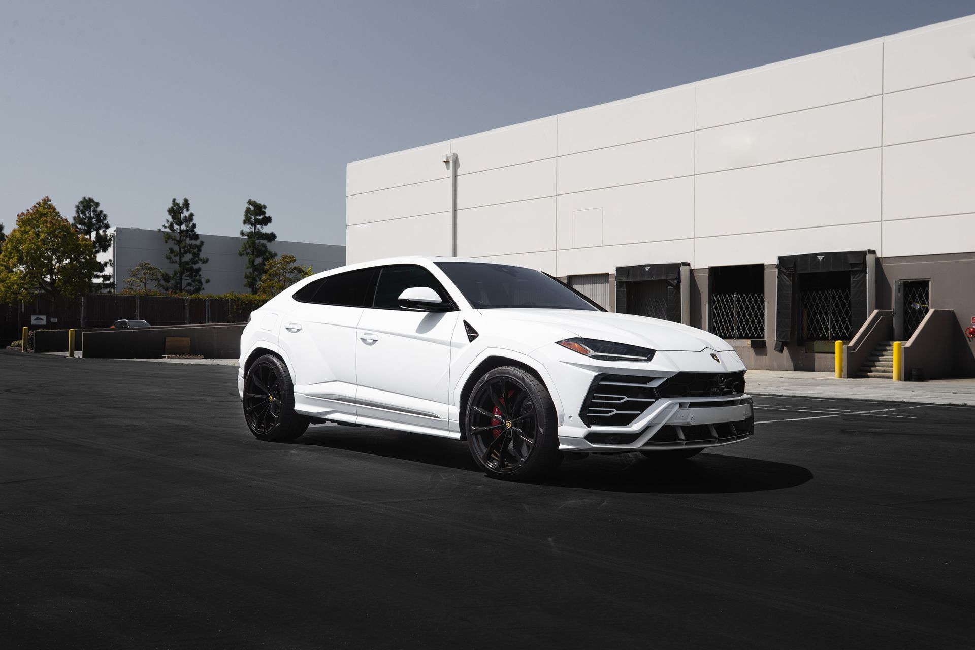 a white lamborghini urus is parked in a parking lot in front of a building .