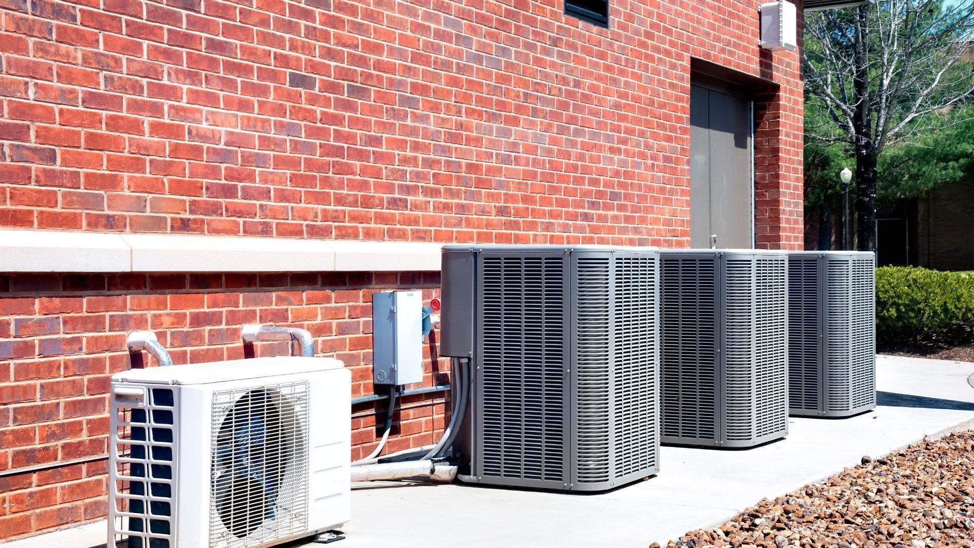 A row of air conditioners are sitting outside of a brick building.