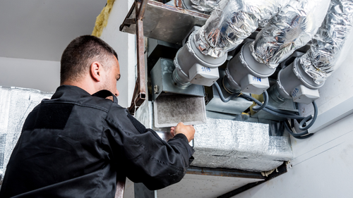 A man is working on a ventilation system in a building.