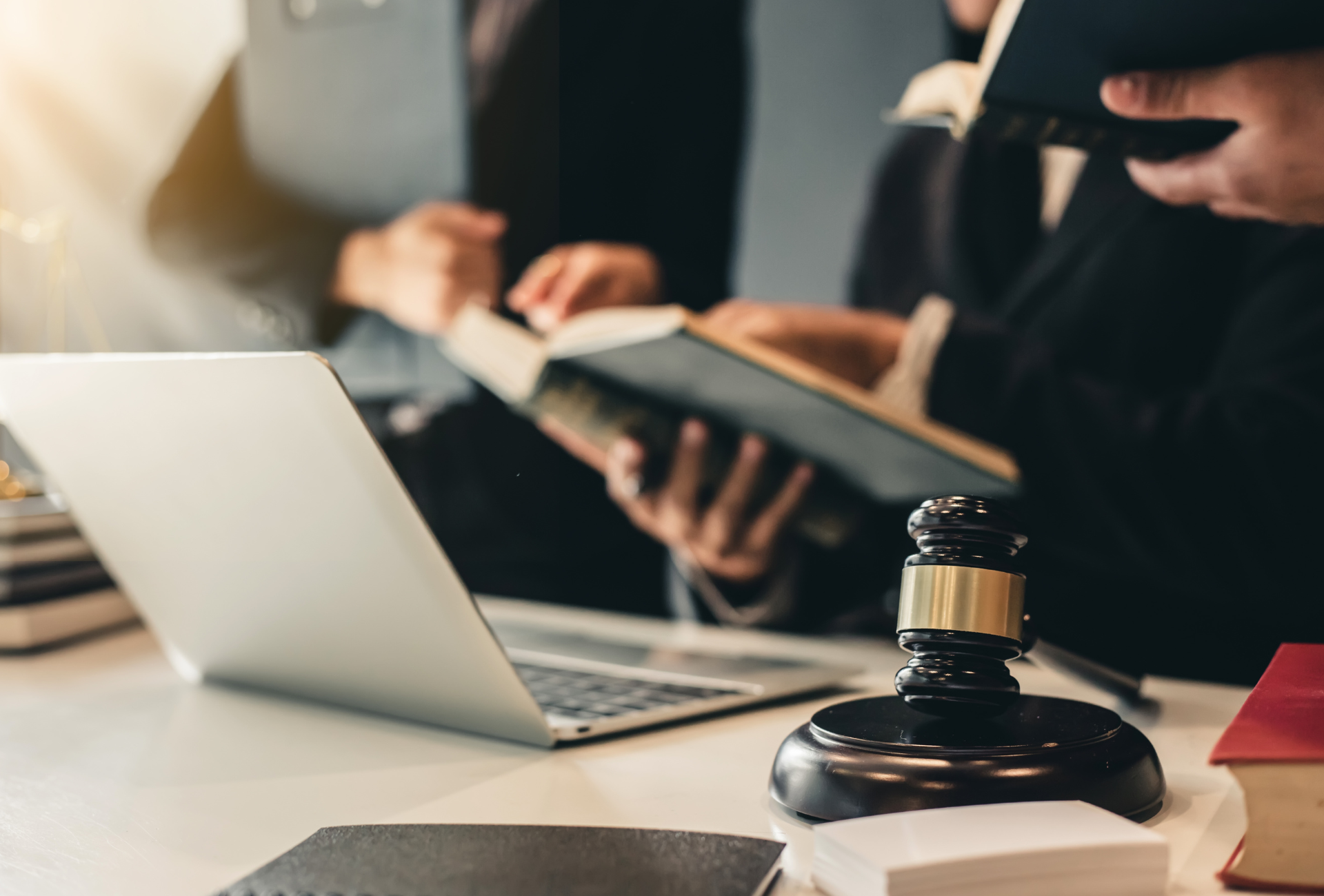 Lawyers reviewing documents and a laptop at a desk, with a gavel in the foreground.