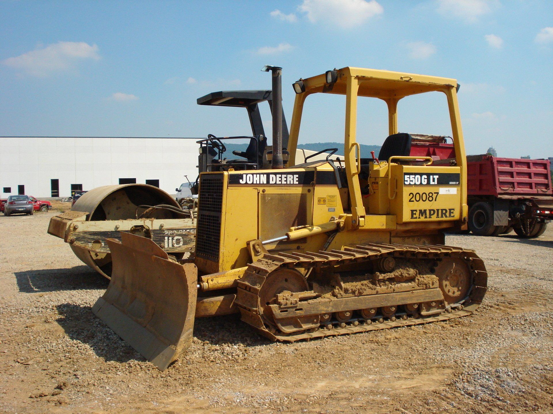 A yellow john deere bulldozer is parked in a dirt lot