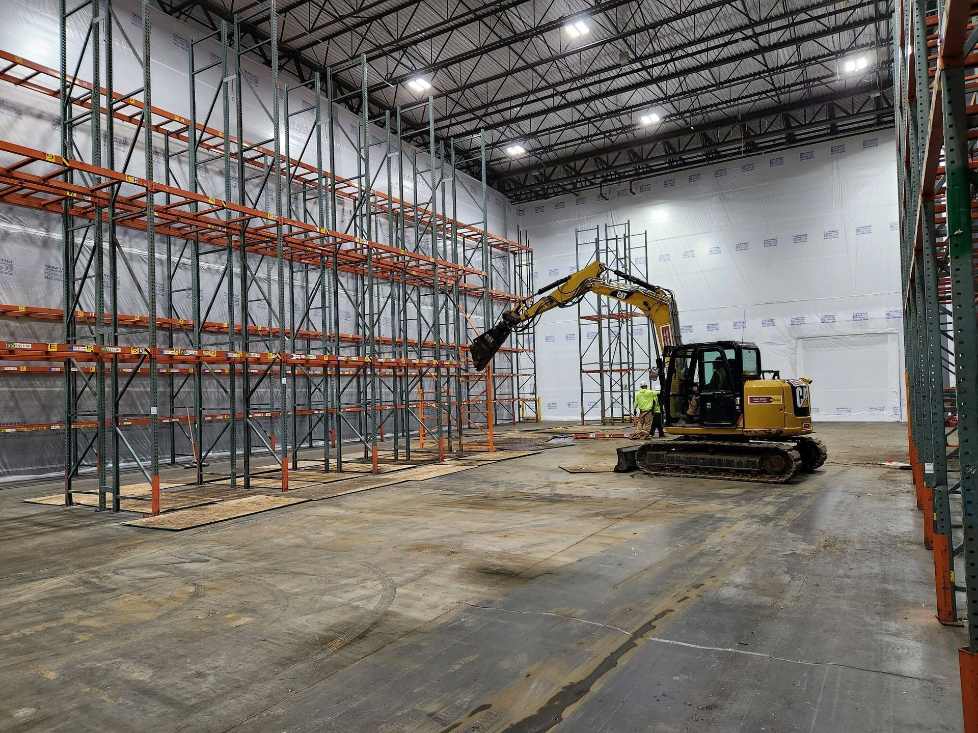 A yellow excavator is working in a large warehouse.