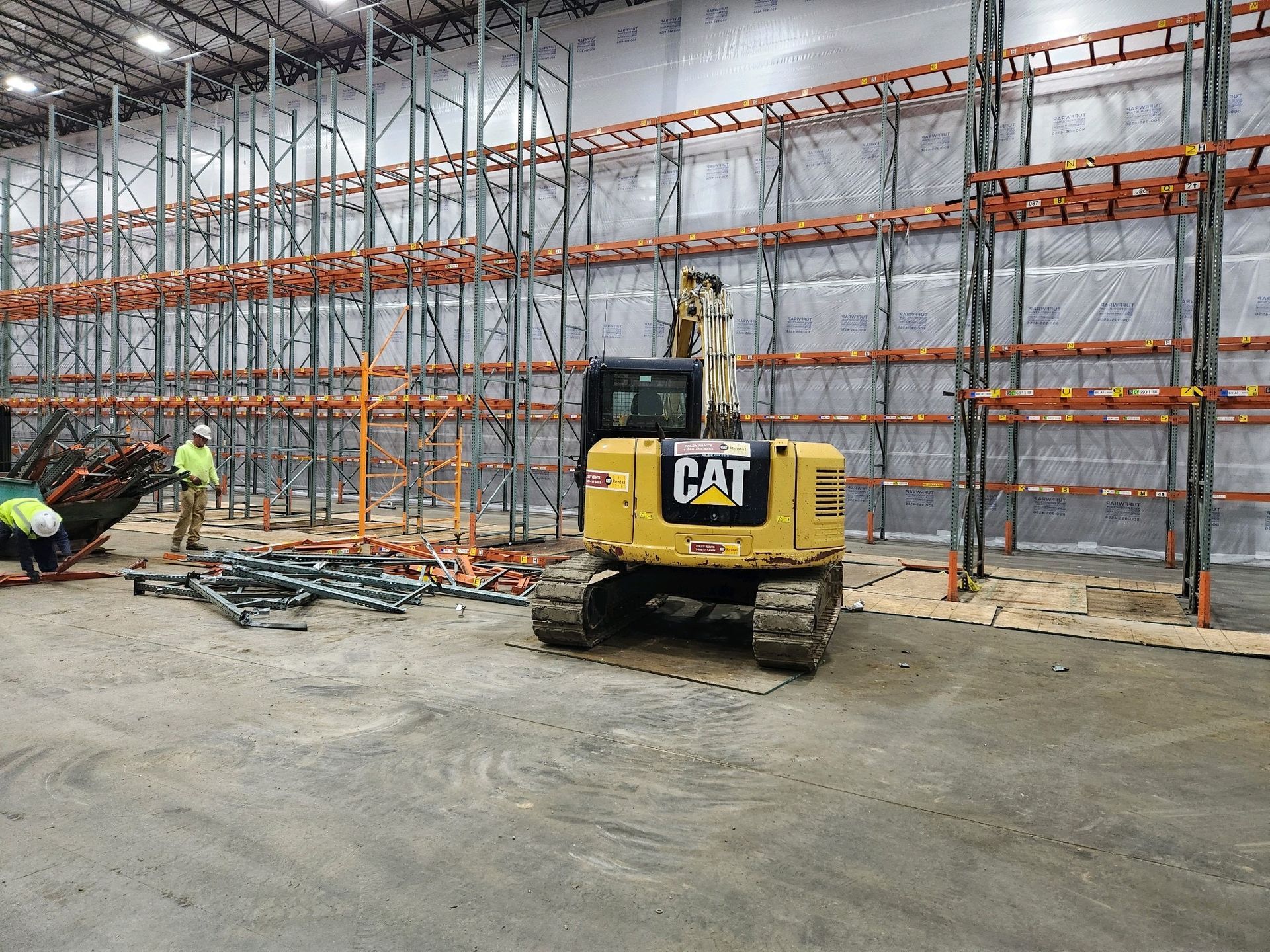 A yellow cat excavator is parked in a large warehouse.