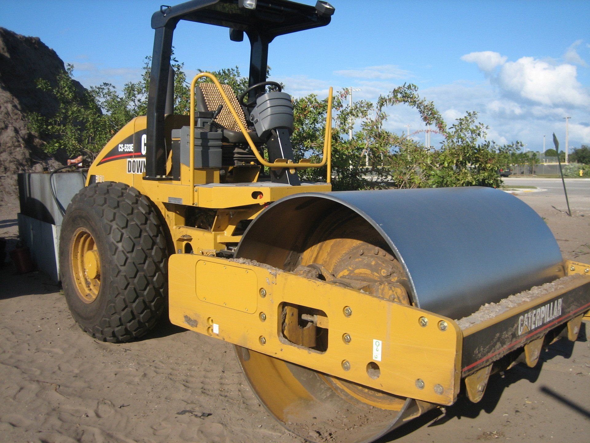 A yellow caterpillar roller is parked in the dirt