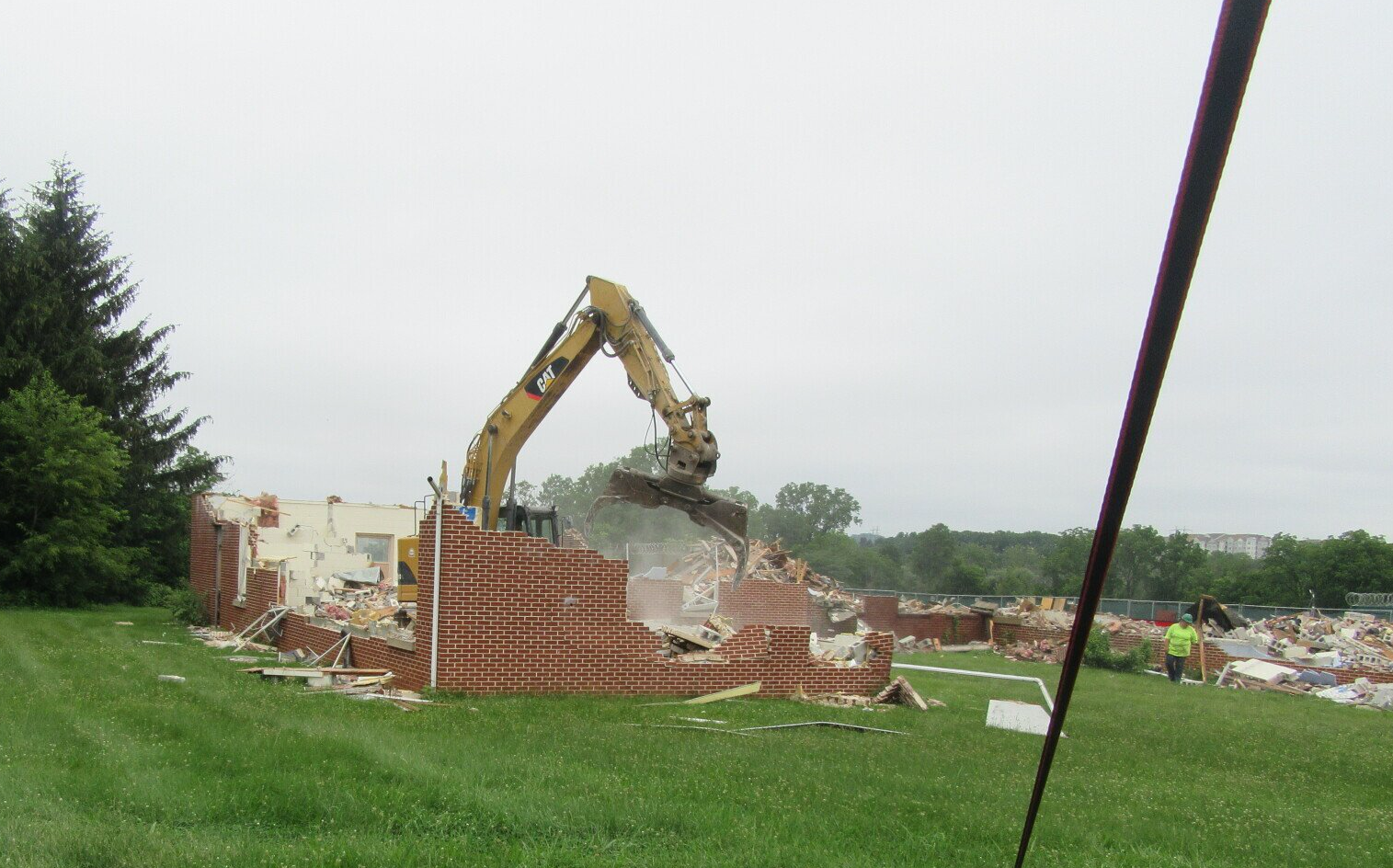 An excavator is demolishing a brick building in a field
