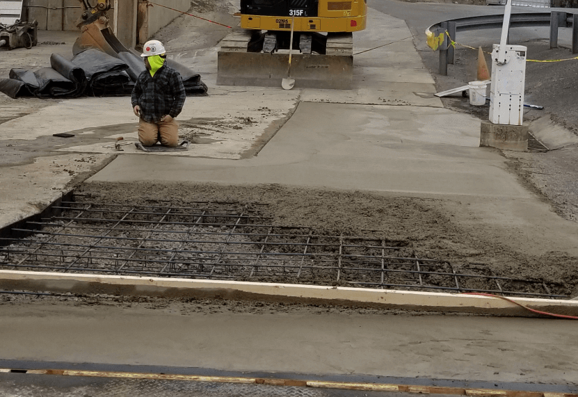 A construction worker is kneeling on a concrete surface.