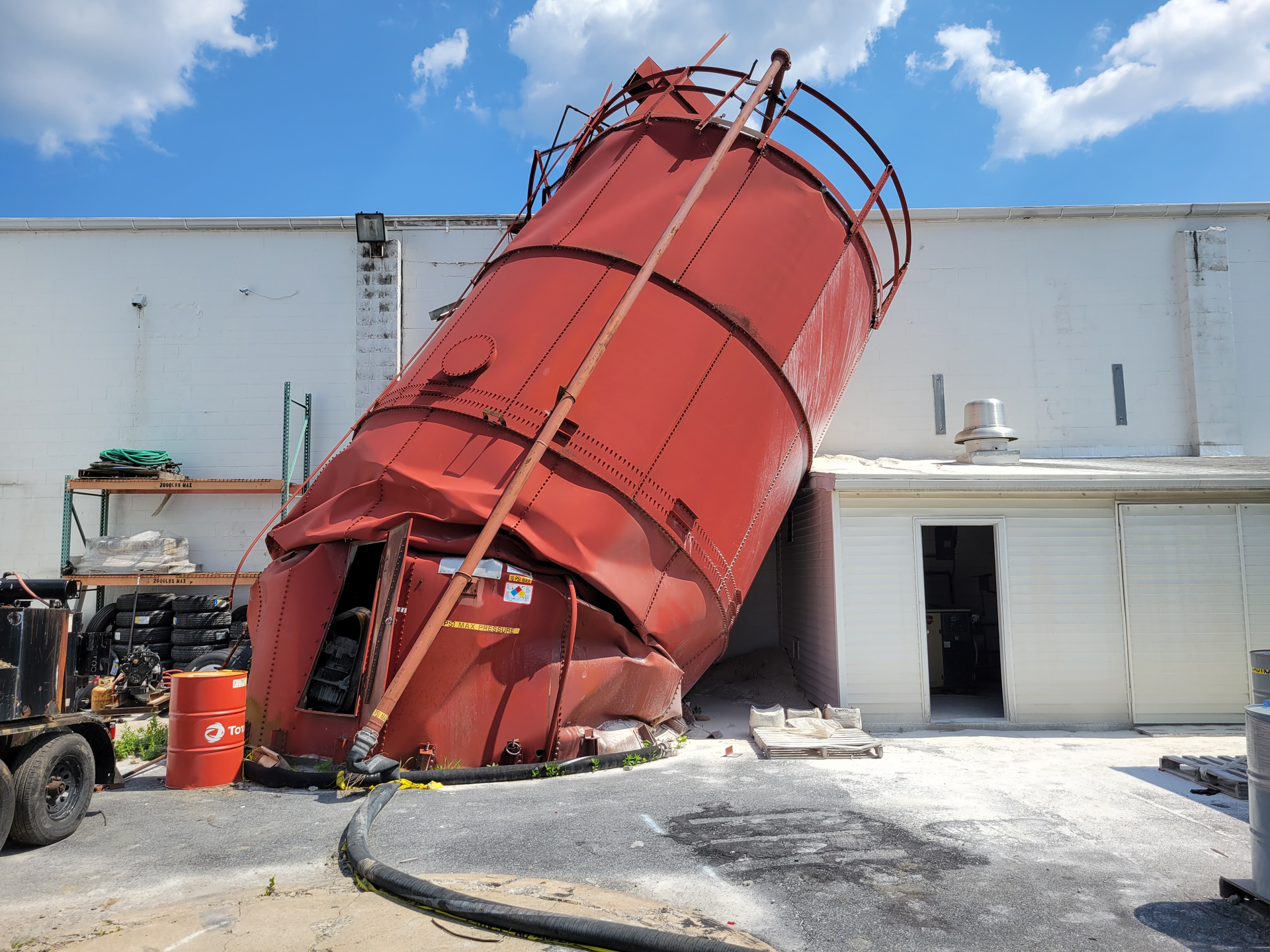 A large red silo is sitting in front of a white building.