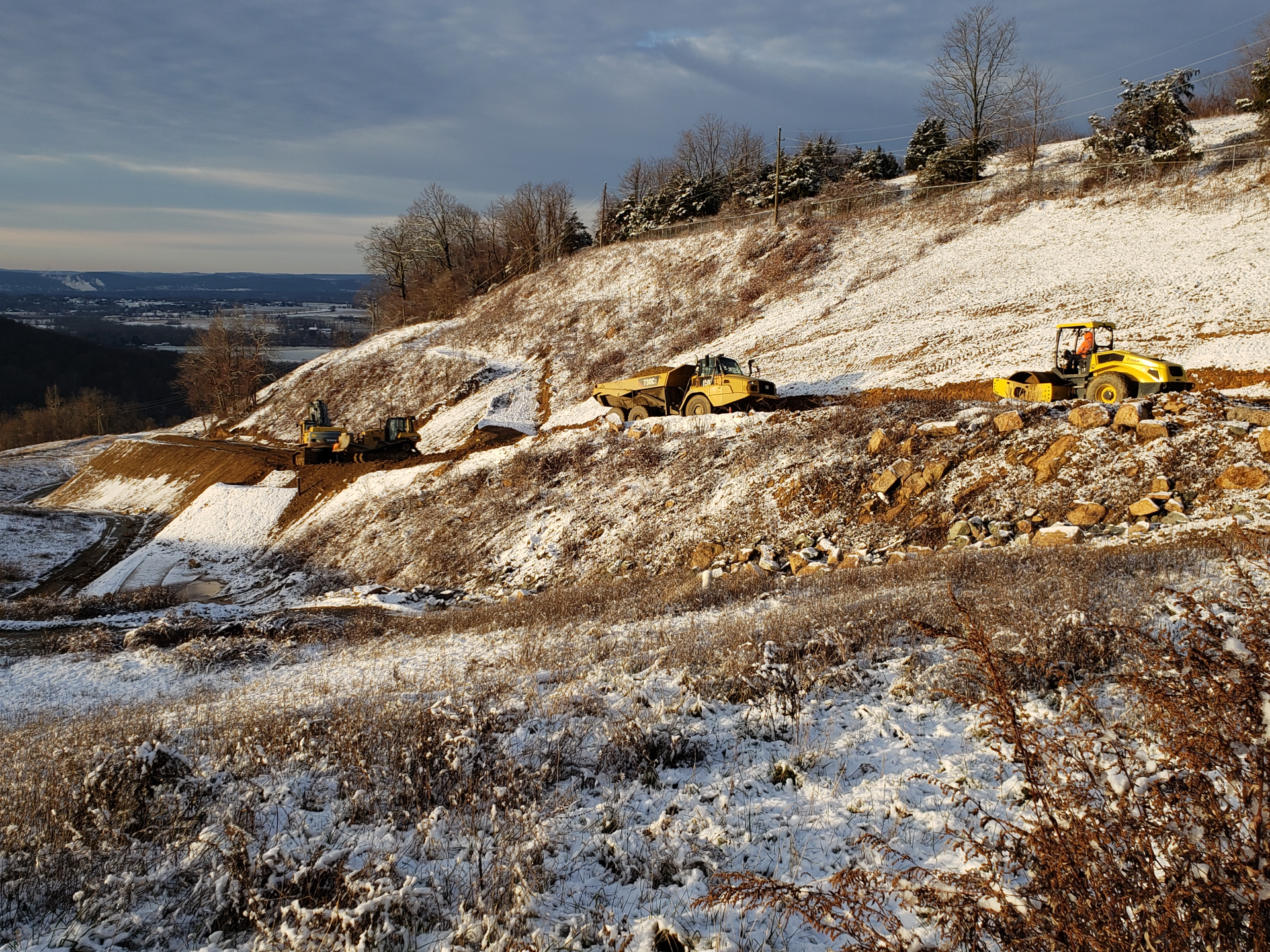 A row of yellow tractors are driving down a snowy hillside.