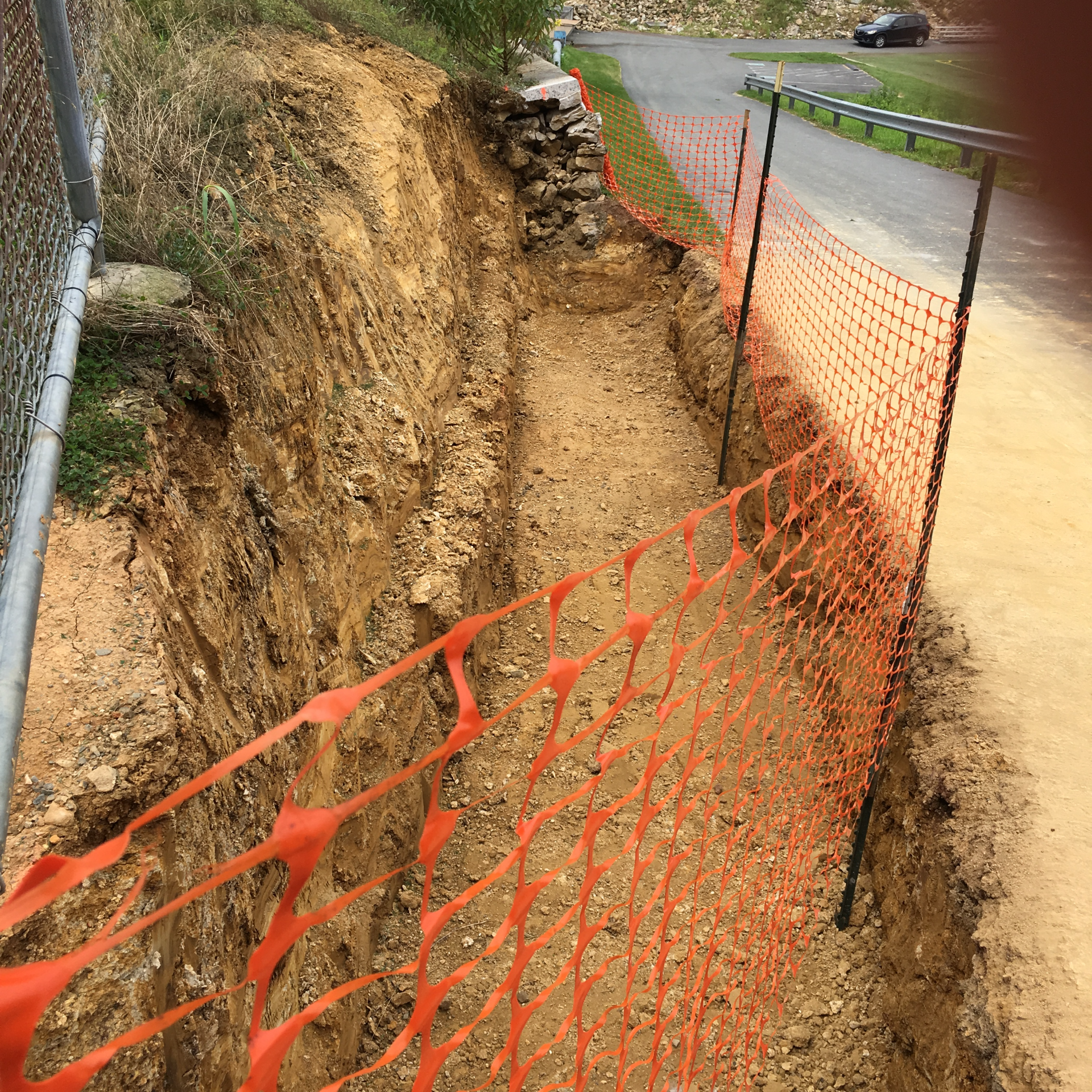 A fence surrounds a trench in the dirt next to a road