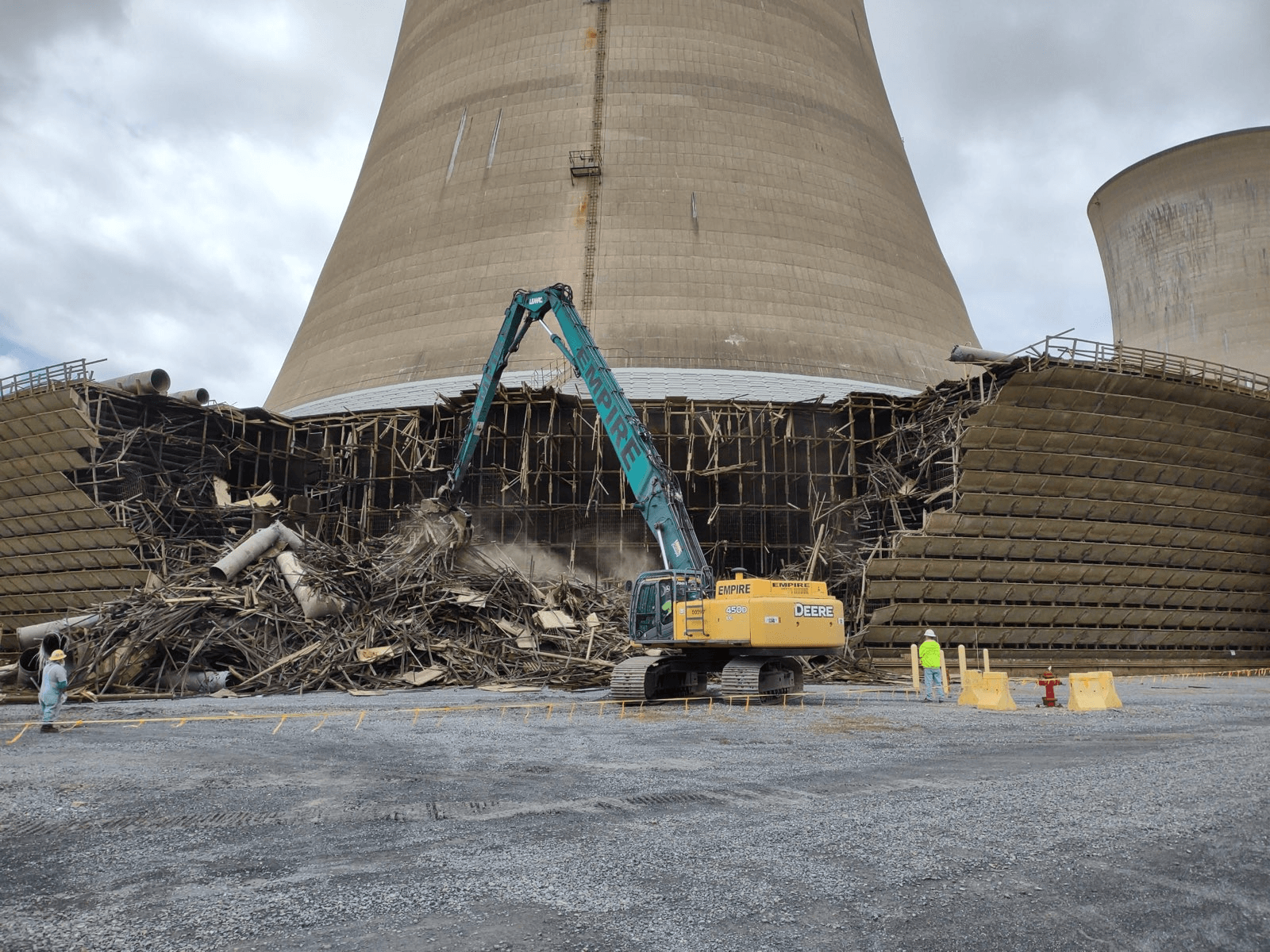 A large cooling tower is being demolished by a crane.