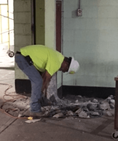 A man wearing a hard hat and a yellow shirt is working on a wall