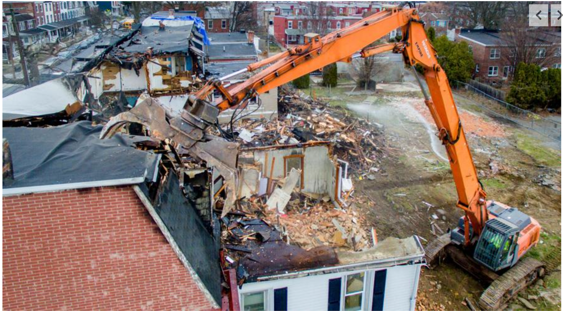 A large orange excavator is demolishing a building.