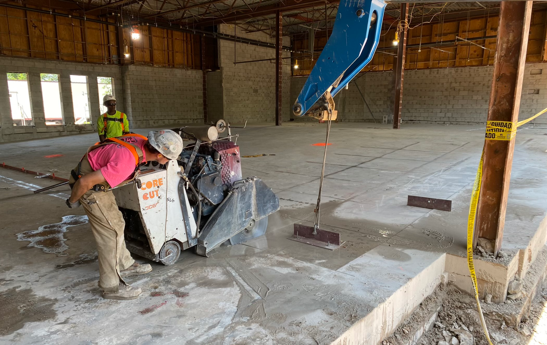 A man is using a machine to cut concrete in a large room.