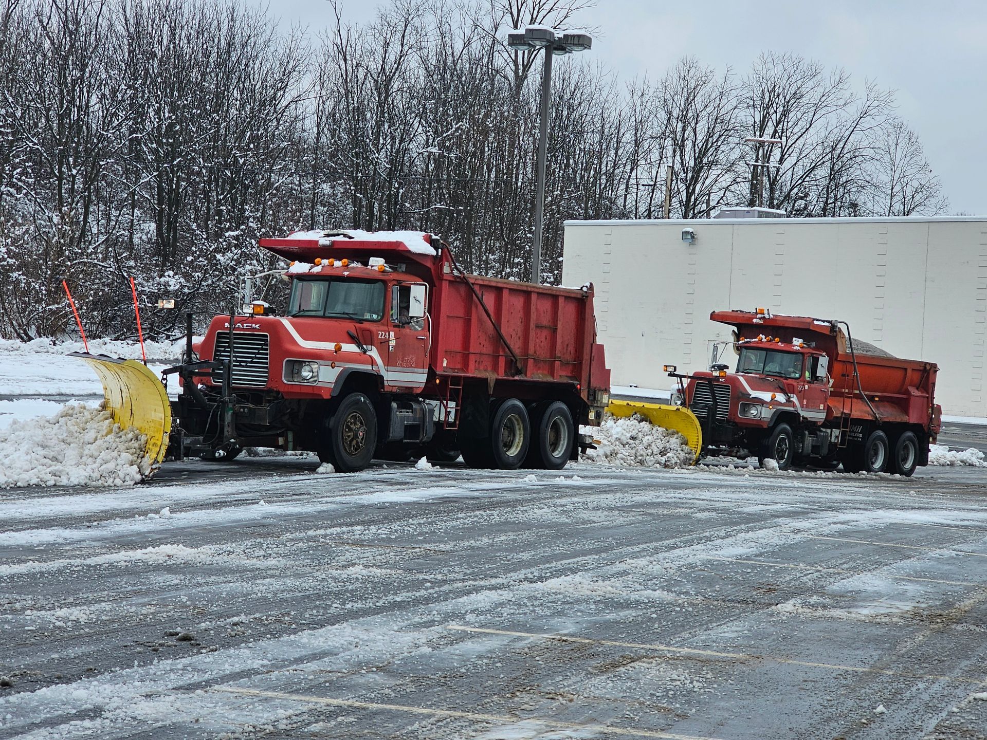 Two snow plows are parked in a parking lot.