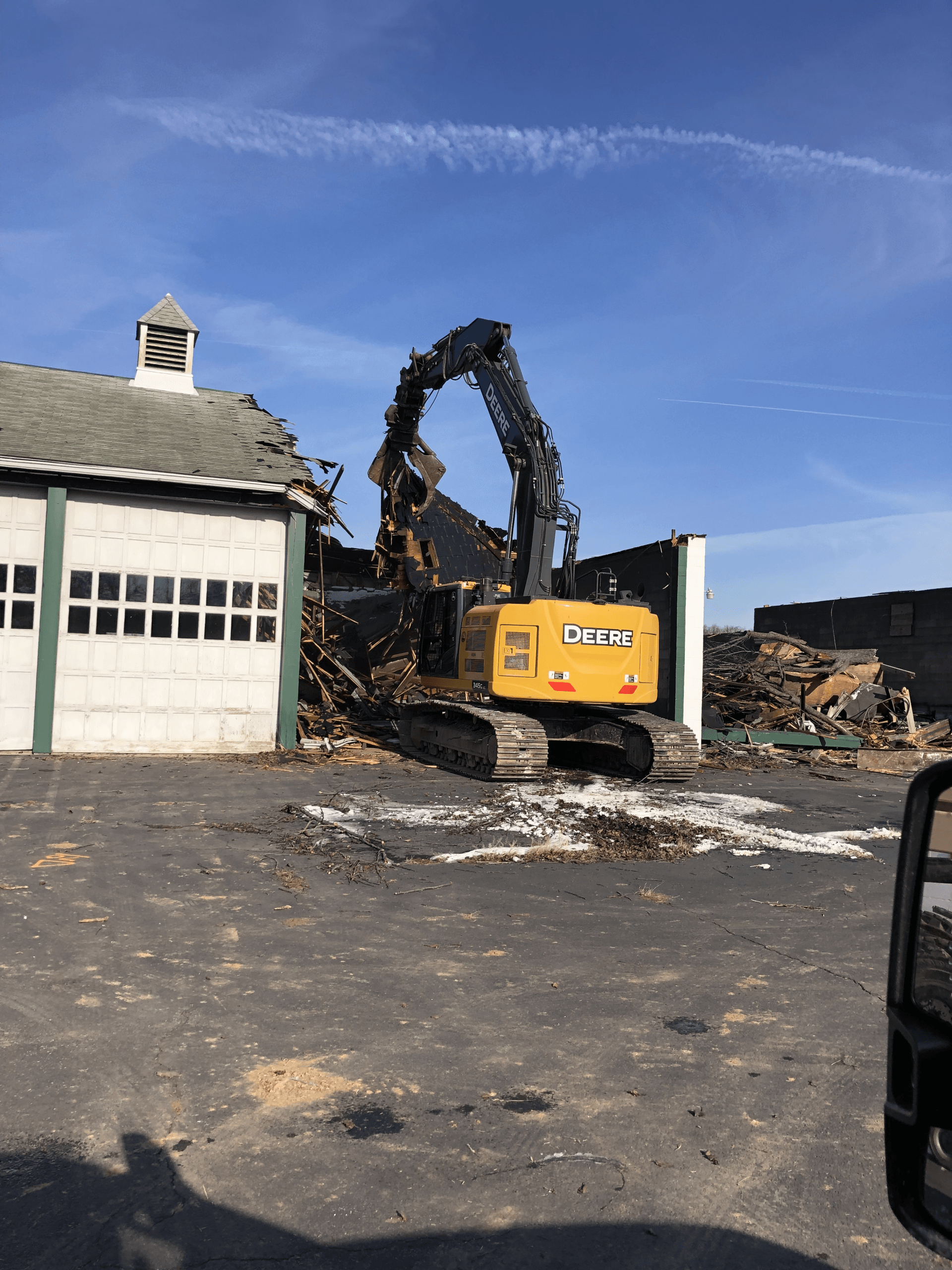 A large excavator is demolishing a building in a parking lot.