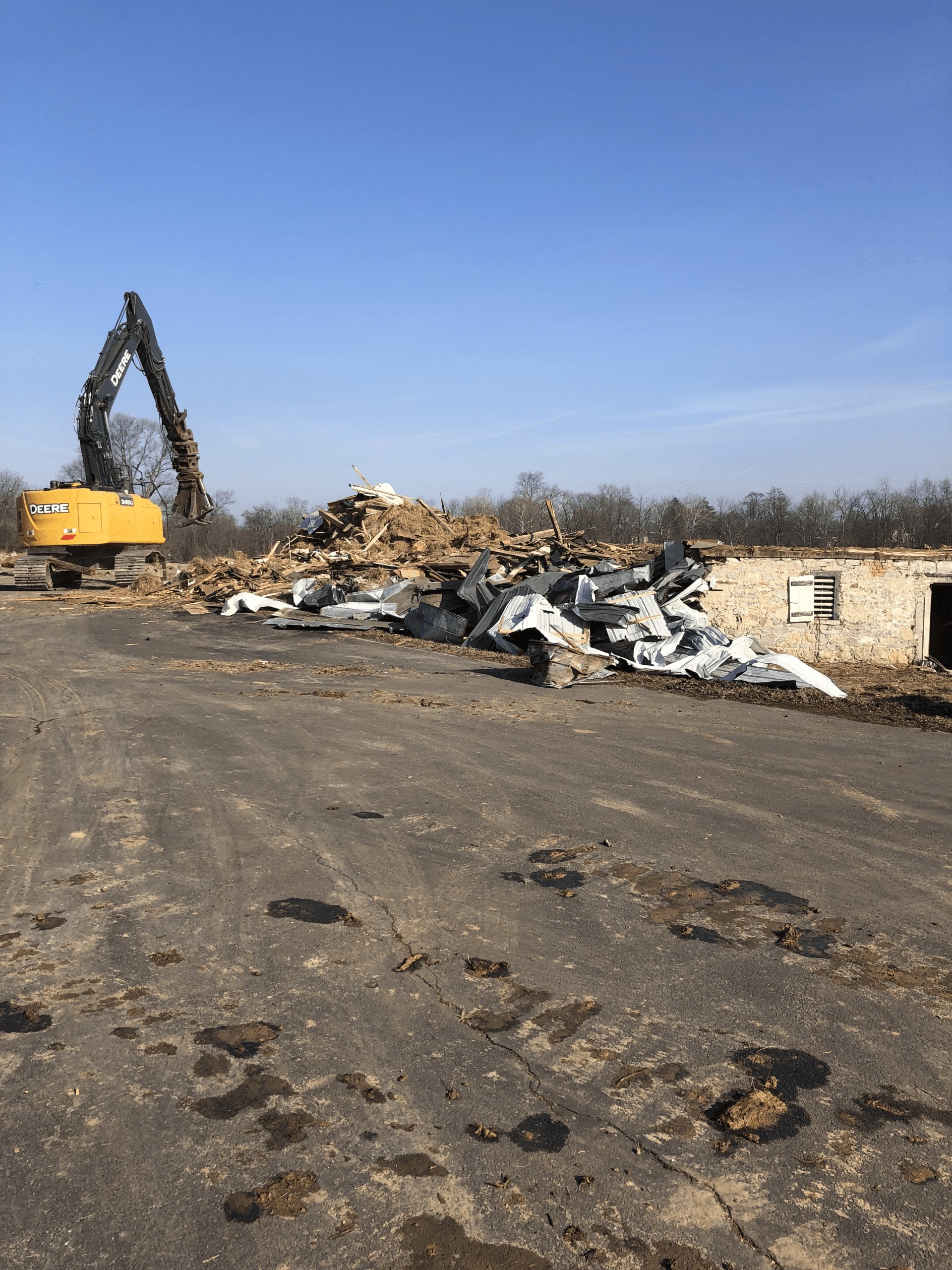 A yellow excavator is moving a pile of scrap metal in a dirt field.