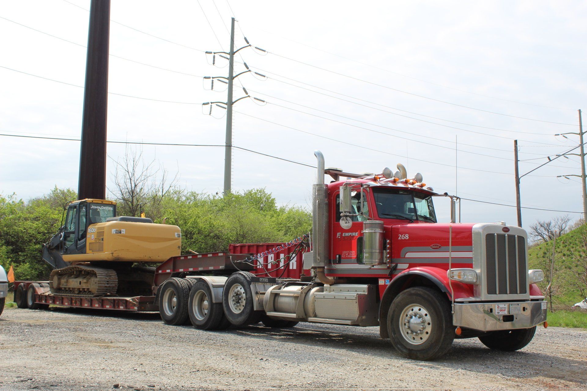 A red semi truck is carrying a yellow excavator