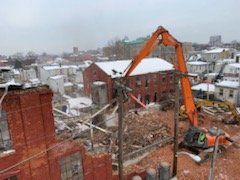 A large orange excavator is demolishing a brick building.