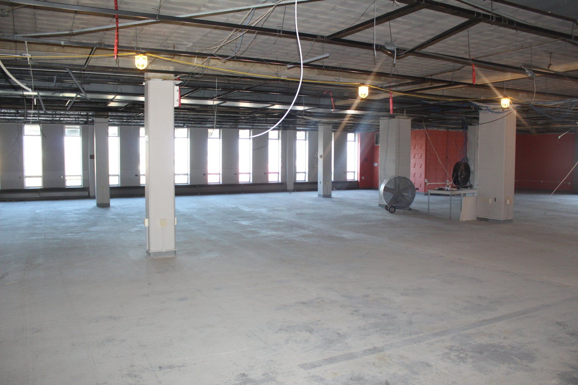 A large empty room with columns and a fan.